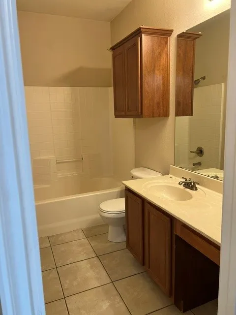 Bathroom featuring a ceramic tile floor, white tub and shower surround, vanity with an integrated sink, and an overhead storage cabinet