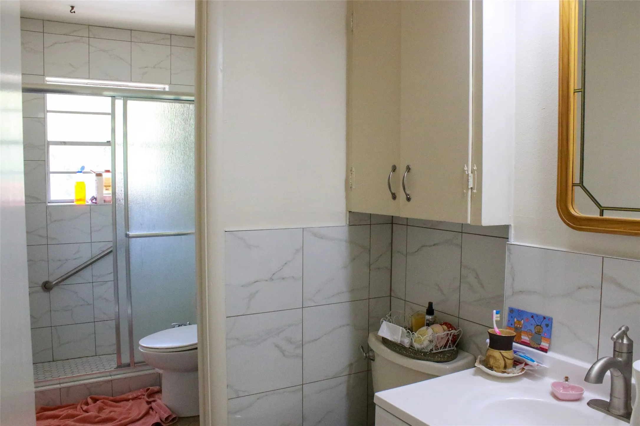 White ceramic tile wall surround, white cabinetry with silver-tone hardware, and a framed mirror