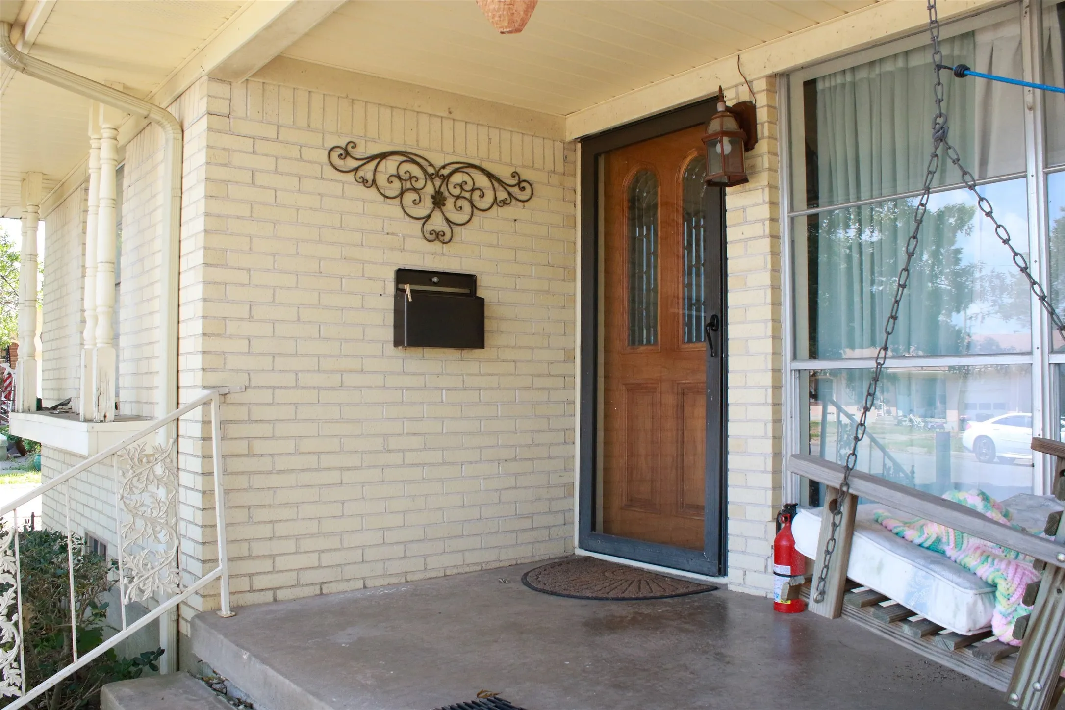 Covered front porch featuring a wood-finish entry door with decorative glass, brick exterior, and decorative wrought iron railing