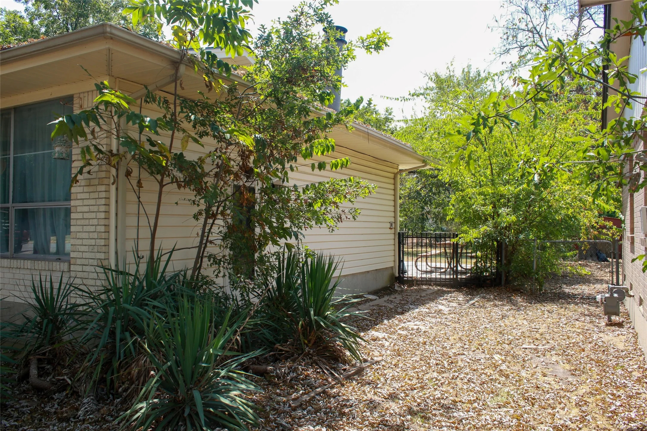 Side yard with a gravel ground cover, a black metal gate, and a brick and siding exterior