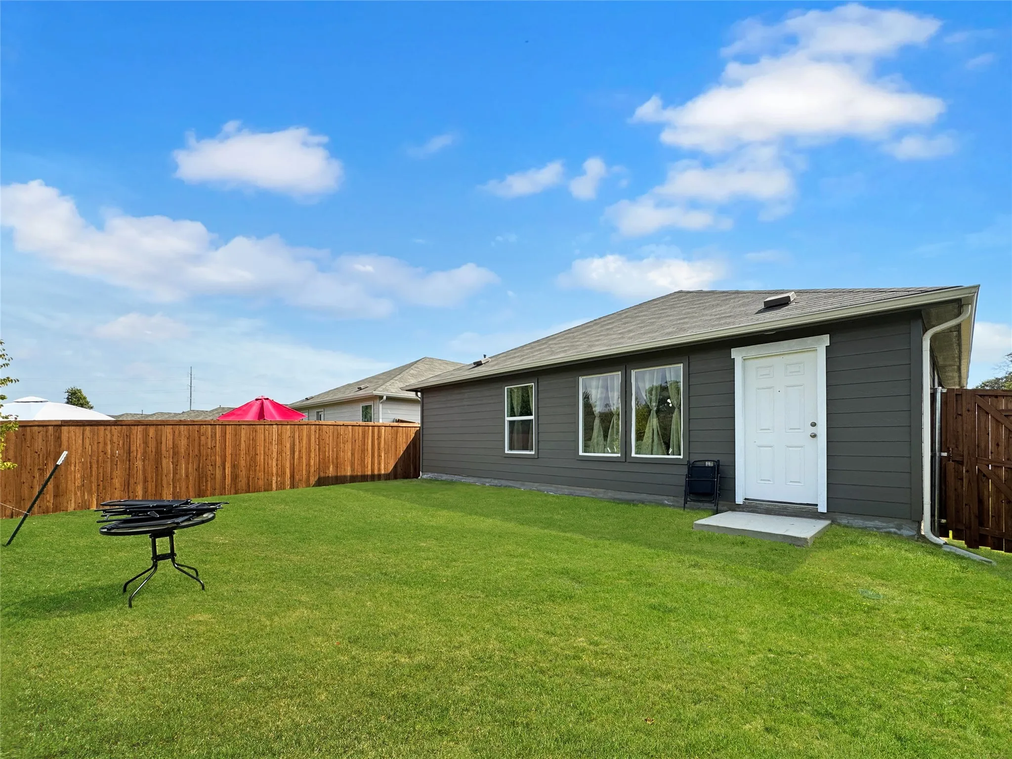 Expansive green lawn, dark gray exterior siding, white trim, wood fence, and a white exterior door