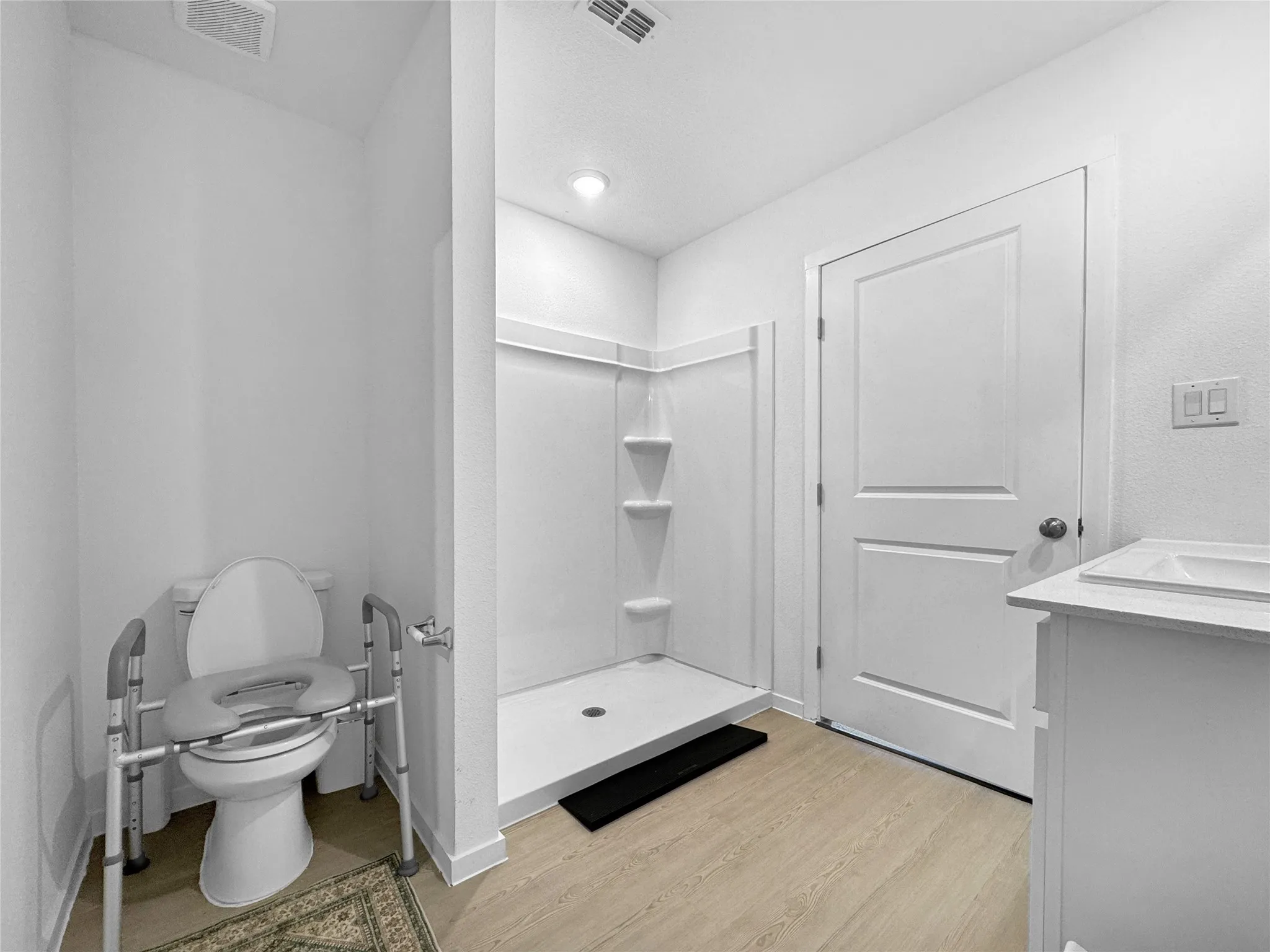 Compact bathroom featuring a white vanity with integrated sink, a walk-in shower with built-in shelving, and wood-finish flooring