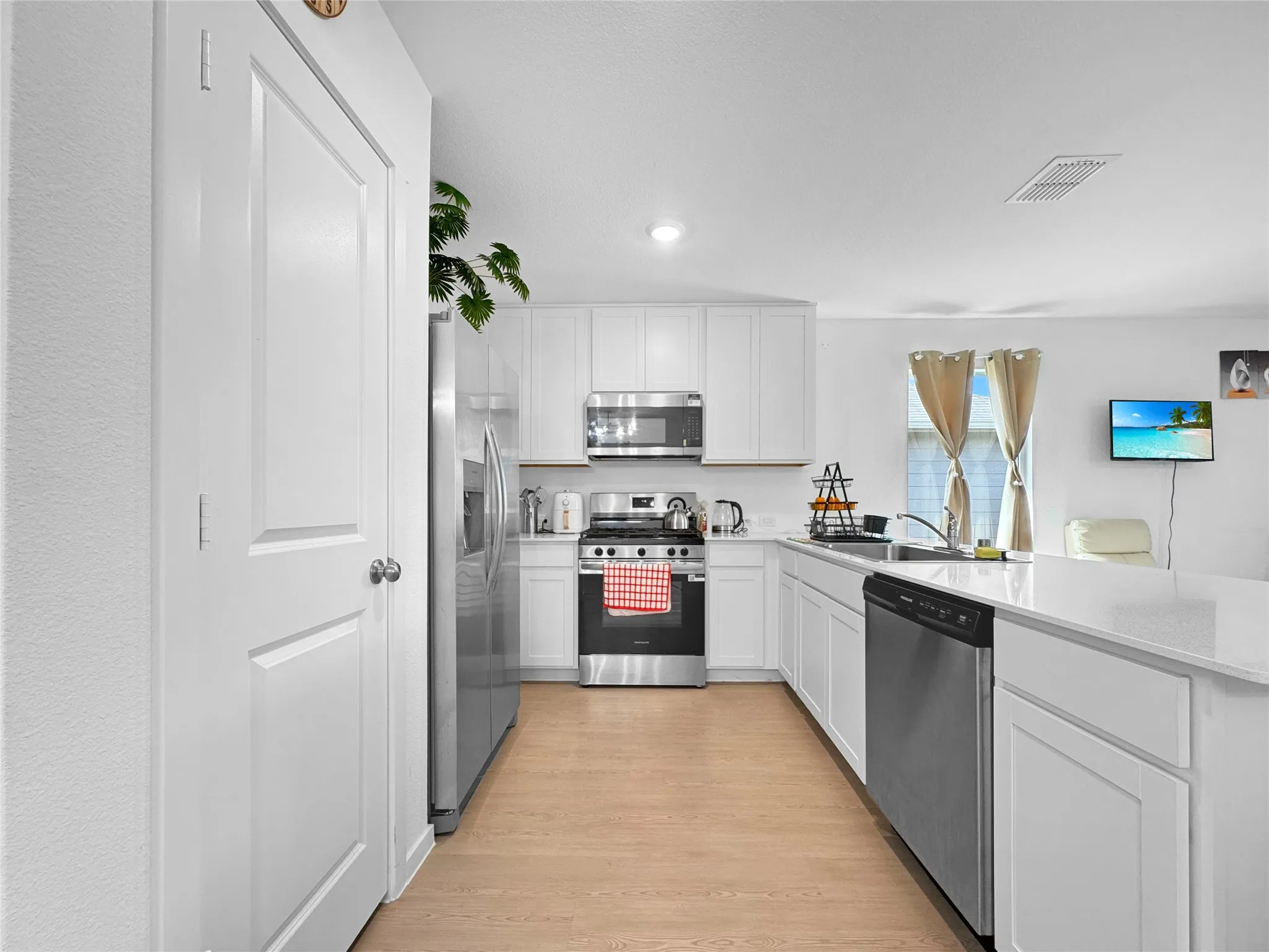 White cabinetry with stainless steel appliances, wood-finish flooring, and light countertops