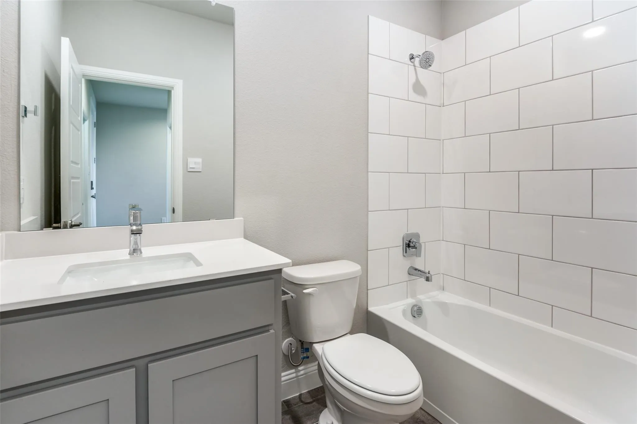 Bathroom featuring a white subway tile shower surround, a built-in bathtub, a toilet, a vanity with a white countertop and an undermount sink, and wood-finish flooring