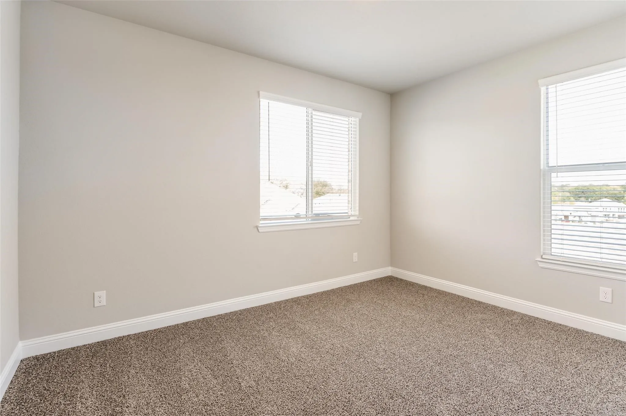 Neutral-toned walls, plush carpet flooring, two windows with blinds, and white trim accents