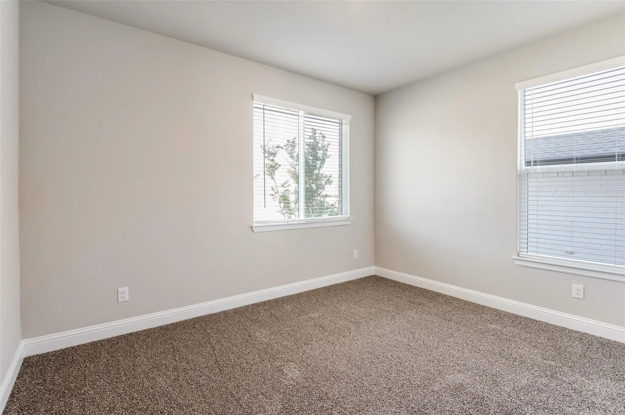 Neutral wall paint, plush carpet flooring, and two windows with blinds