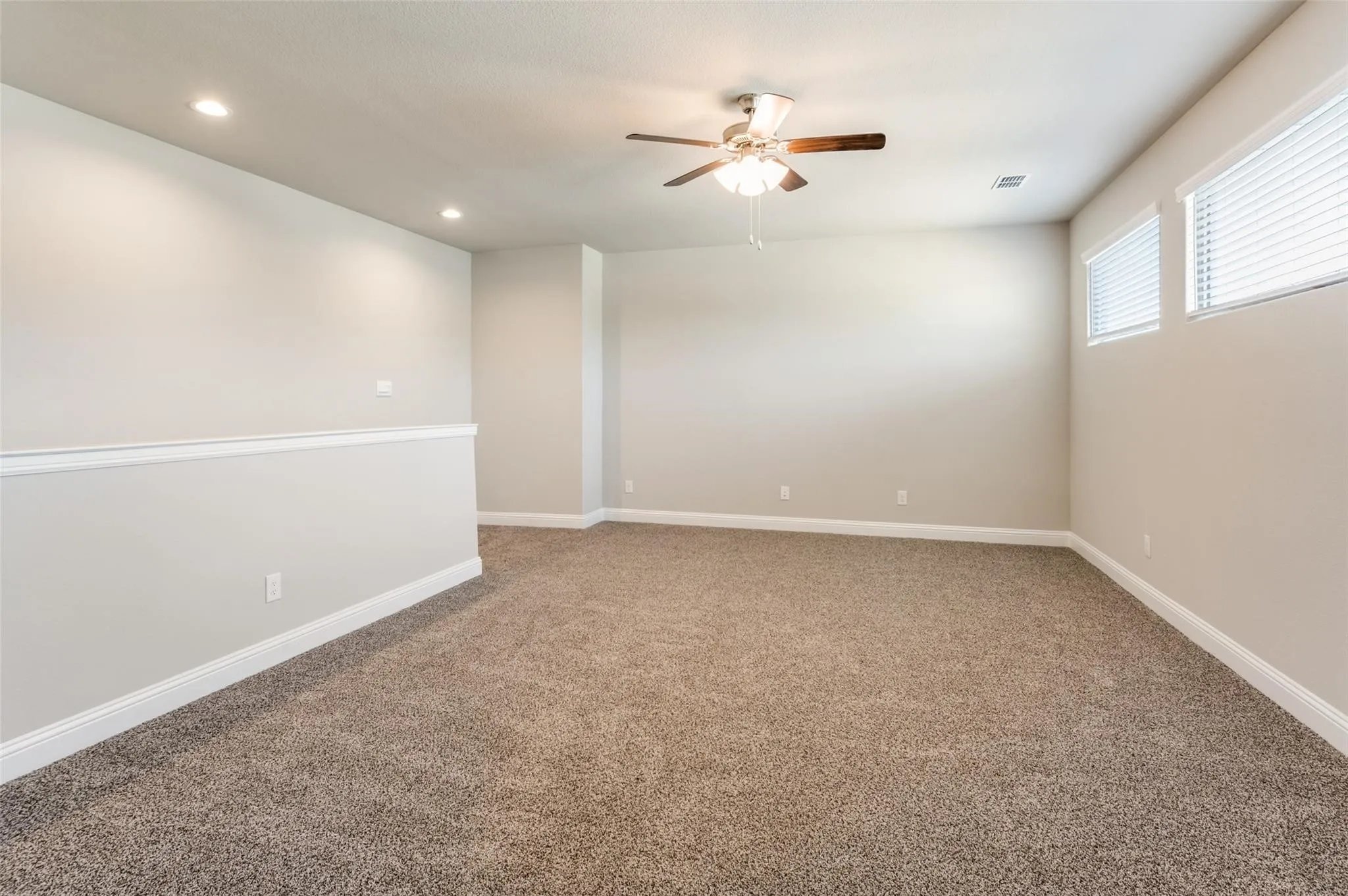 Spacious carpeted room featuring recessed lighting, a ceiling fan, and multiple windows with blinds