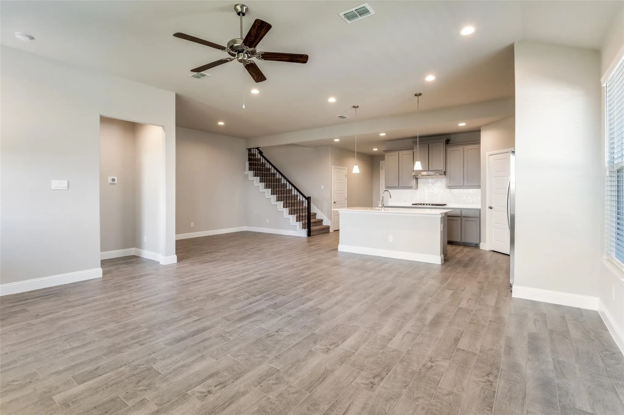 Expansive space featuring wood-finish flooring, a kitchen island with pendant lighting, gray cabinetry, and a staircase with a dark metal railing