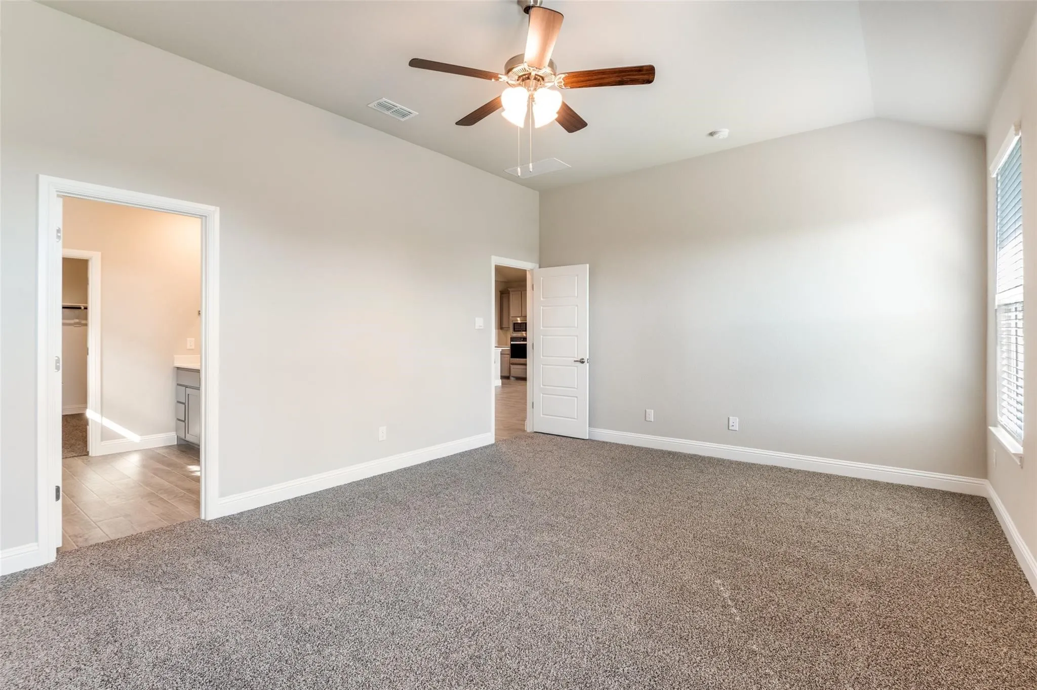 Spacious interior featuring neutral carpeting, a vaulted ceiling, and a ceiling fan with light fixture