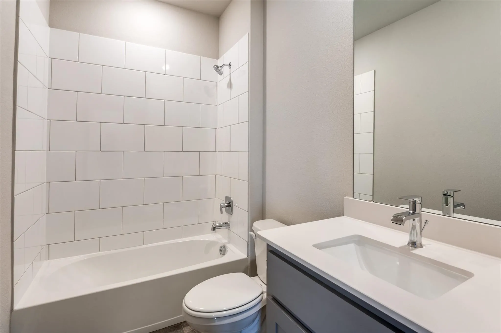 Bathroom featuring a white subway tile tub surround, chrome fixtures, a single vanity with an integrated sink, and a large wall-mounted mirror