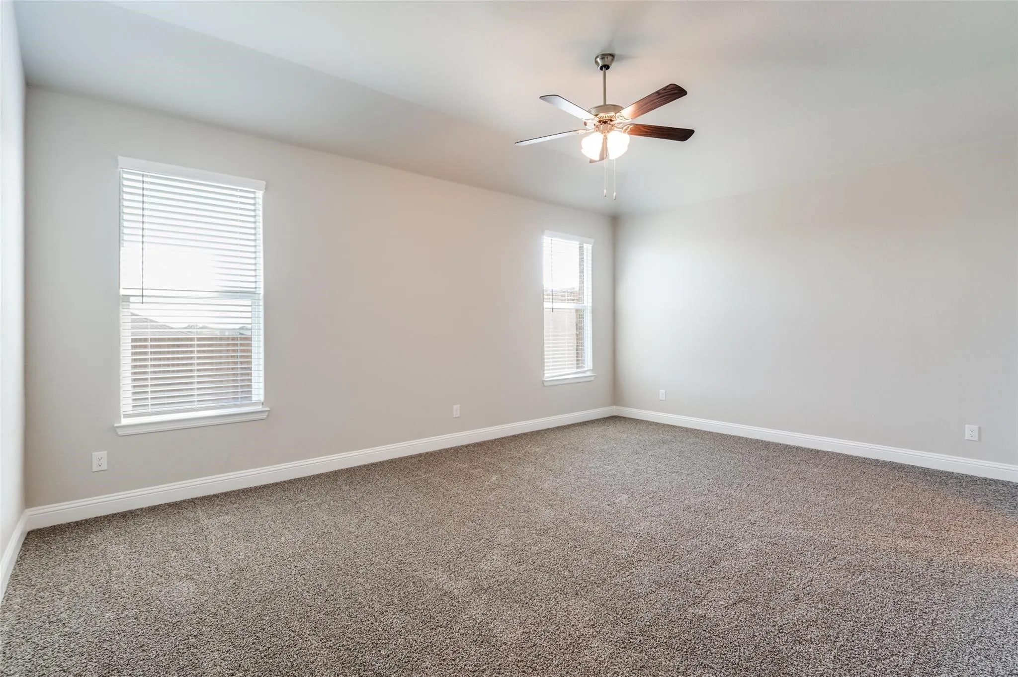Spacious room with neutral wall paint, two windows, textured carpeting, and a ceiling fan with integrated lighting