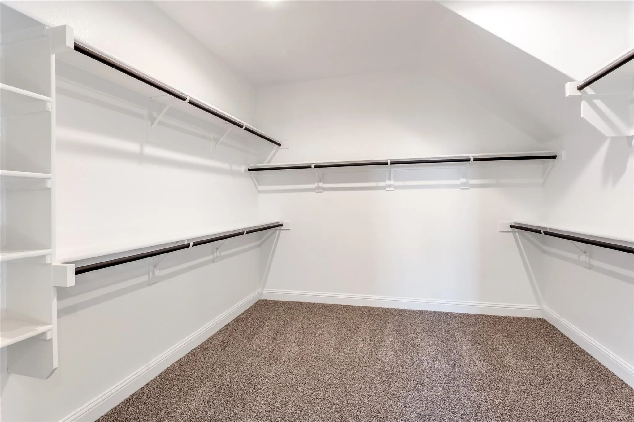 Walk-in closet with integrated shelving, multiple hanging rods, white walls, and carpeting