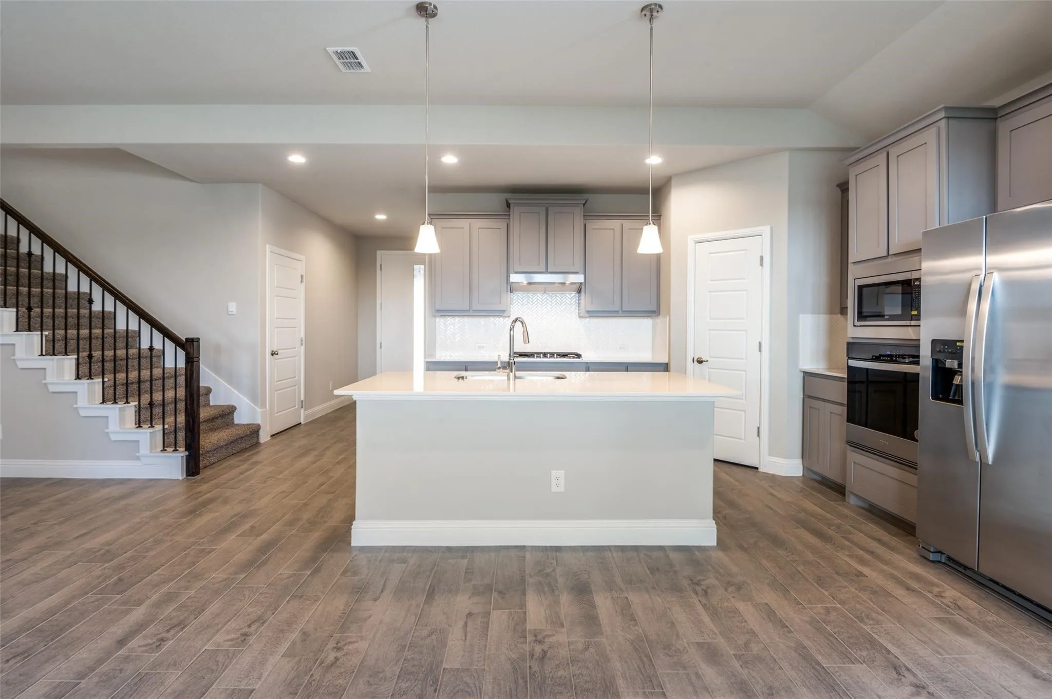 Kitchen island with sink, stainless steel appliances, wood-finish flooring, recessed lighting, and a staircase with metal balusters