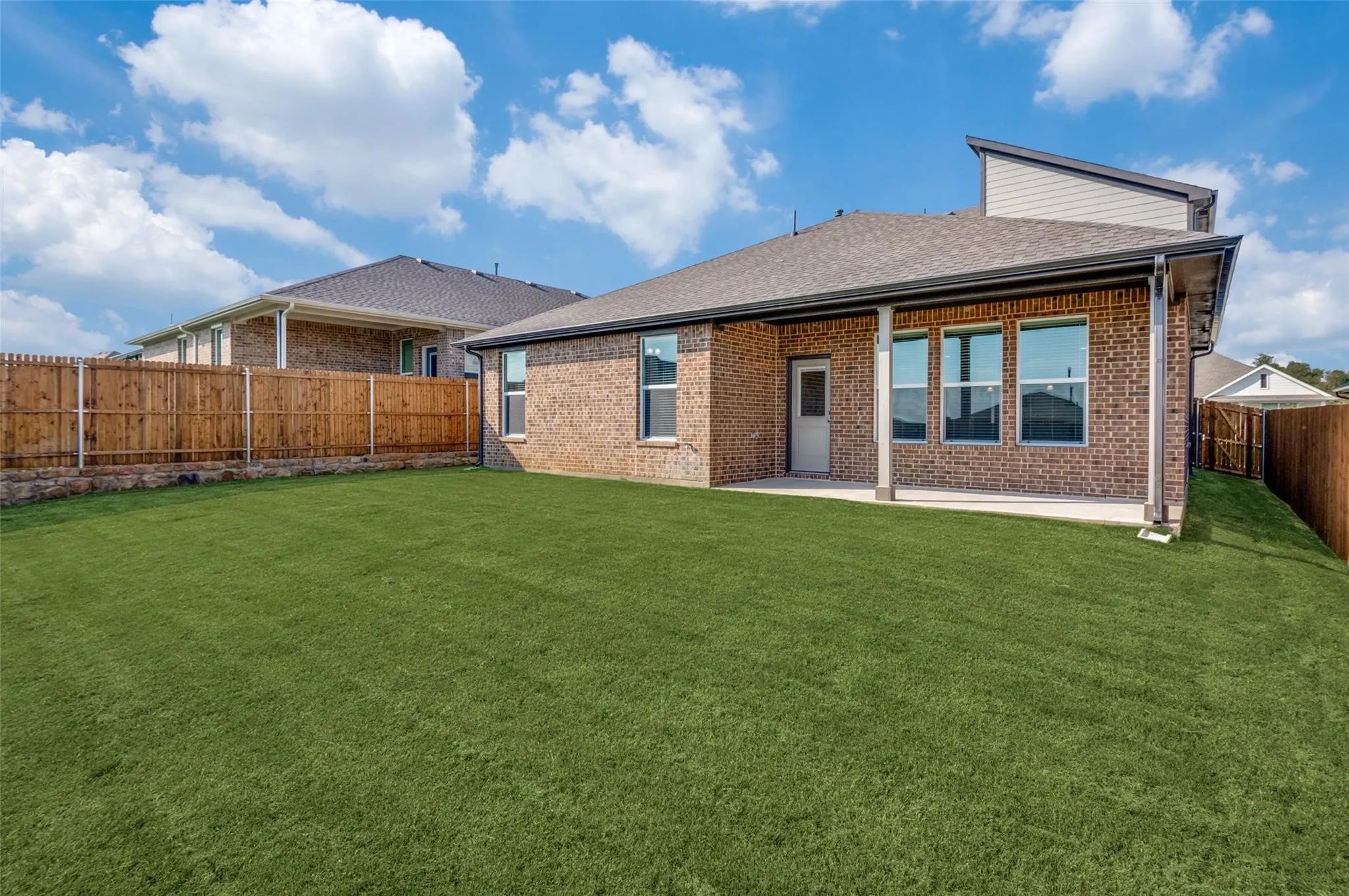 Expansive grassy yard with a covered patio, brick exterior, and wood fencing