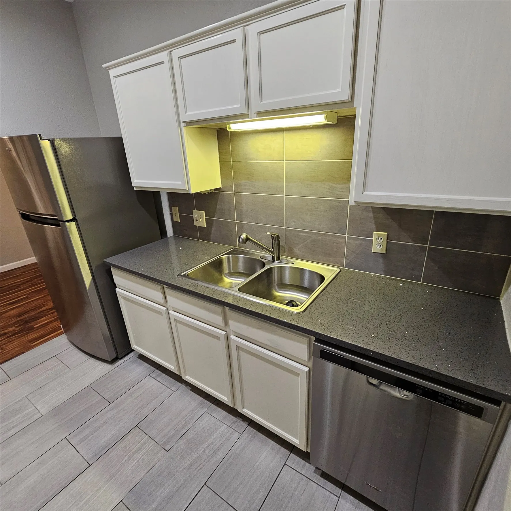 Kitchen with appliances with stainless steel finishes, wood finish floors, white cabinets, backsplash, and dark countertops