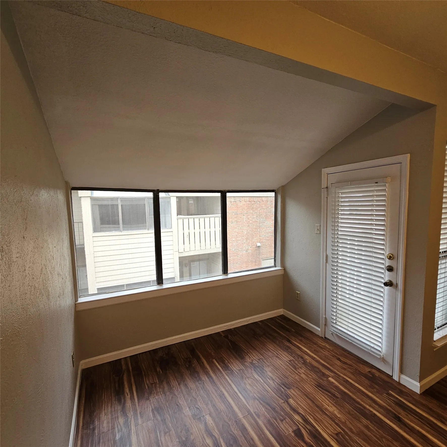 Spare room featuring vaulted ceiling and dark wood-style floors