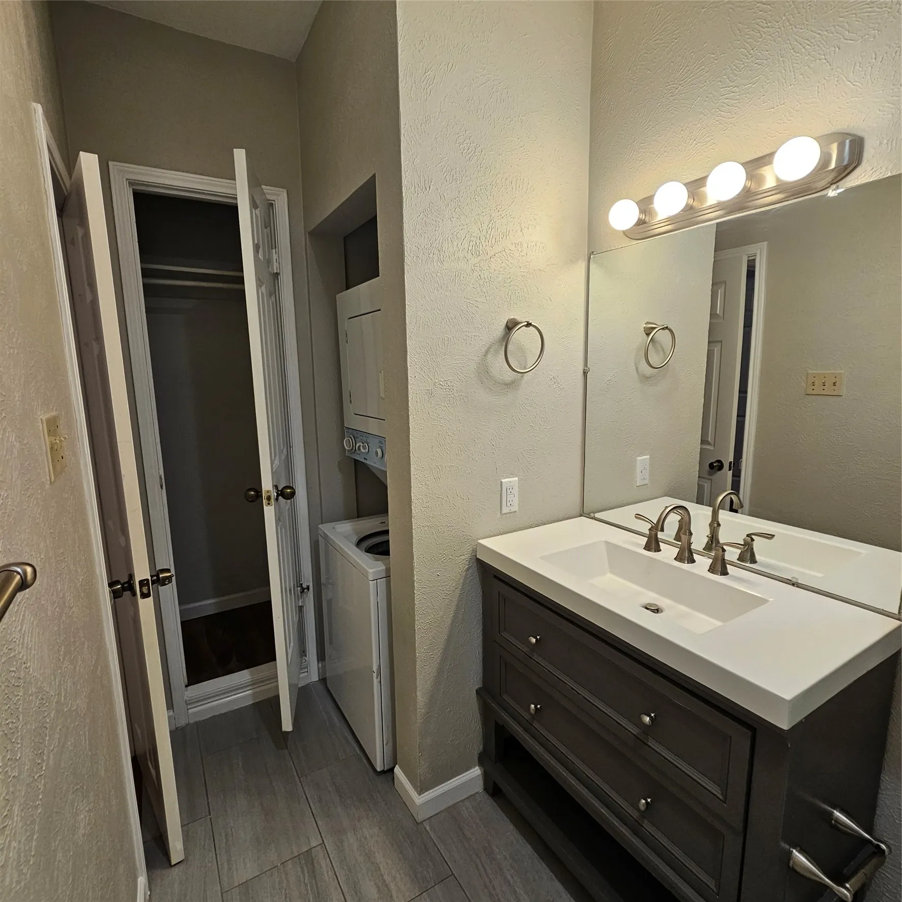 Bathroom with vanity, wood finished floors, a textured wall, and stacked washing machine and dryer