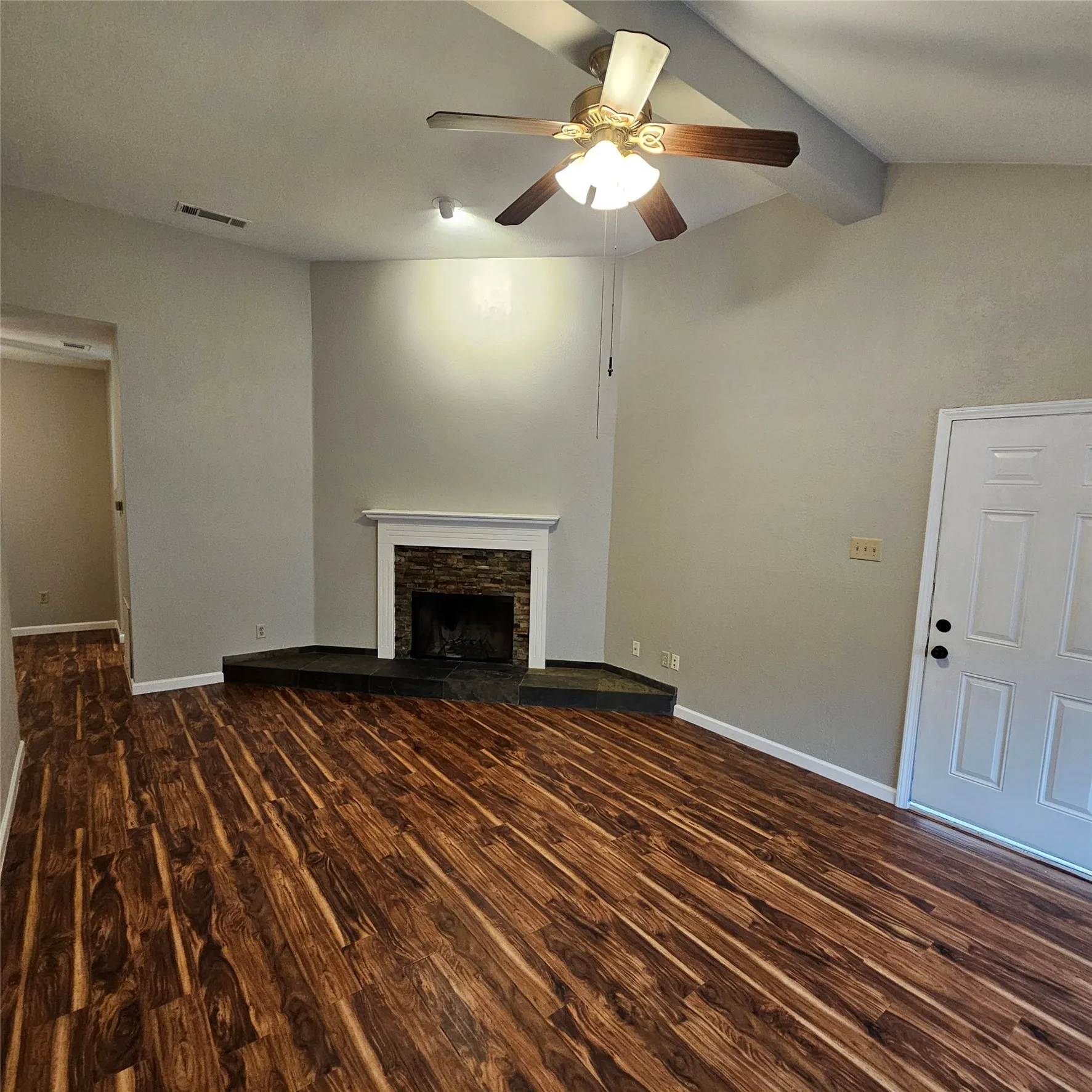 Unfurnished living room with wood finished floors, a ceiling fan, and a stone fireplace