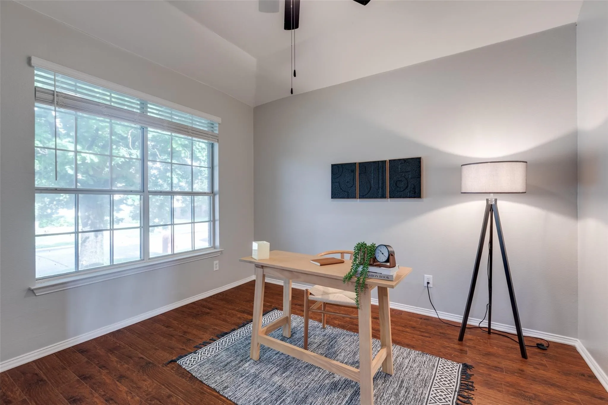 Spacious room featuring multiple windowpanes, wood-finish flooring, light gray wall paint, and a ceiling fan