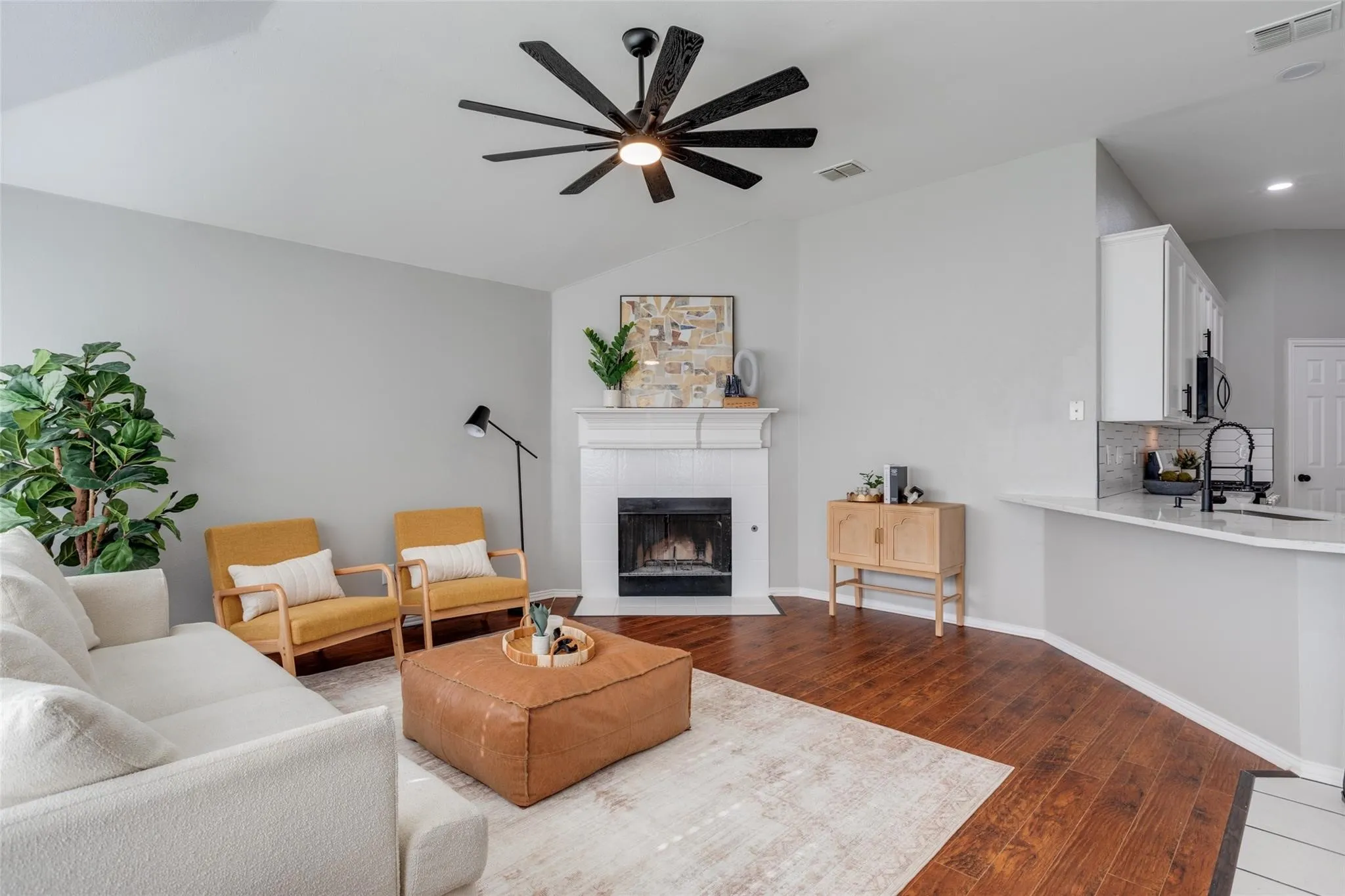 Vaulted ceiling living area featuring wood-finish flooring, a contemporary fireplace with a white mantel, and a ceiling fan