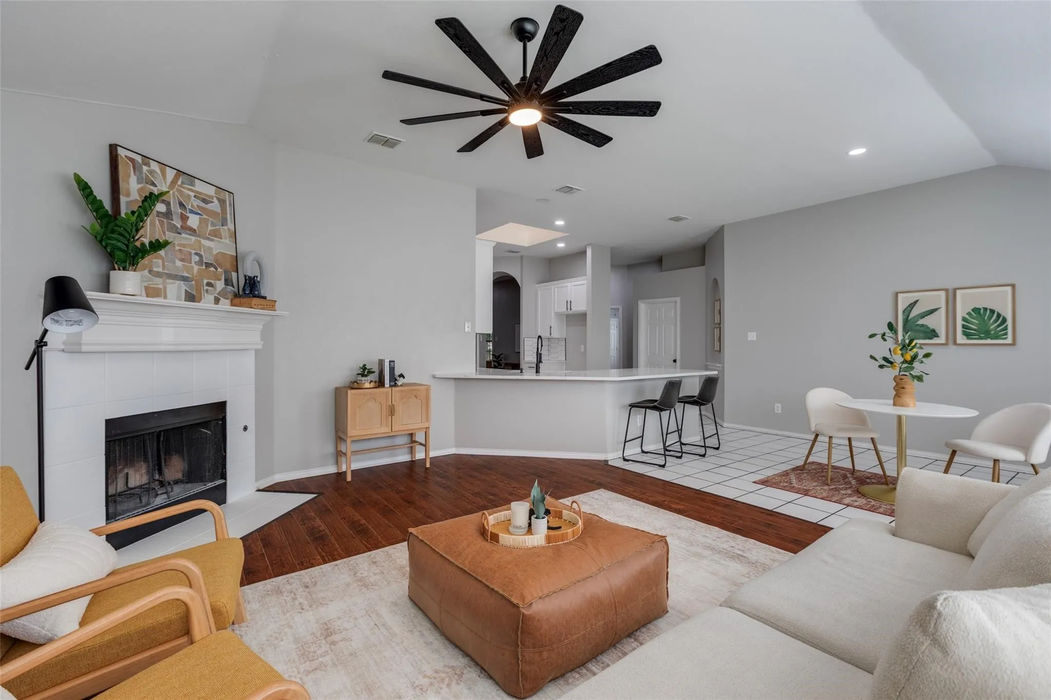 Spacious living area featuring wood-finish flooring, a white brick fireplace with mantel, and a prominent ceiling fan