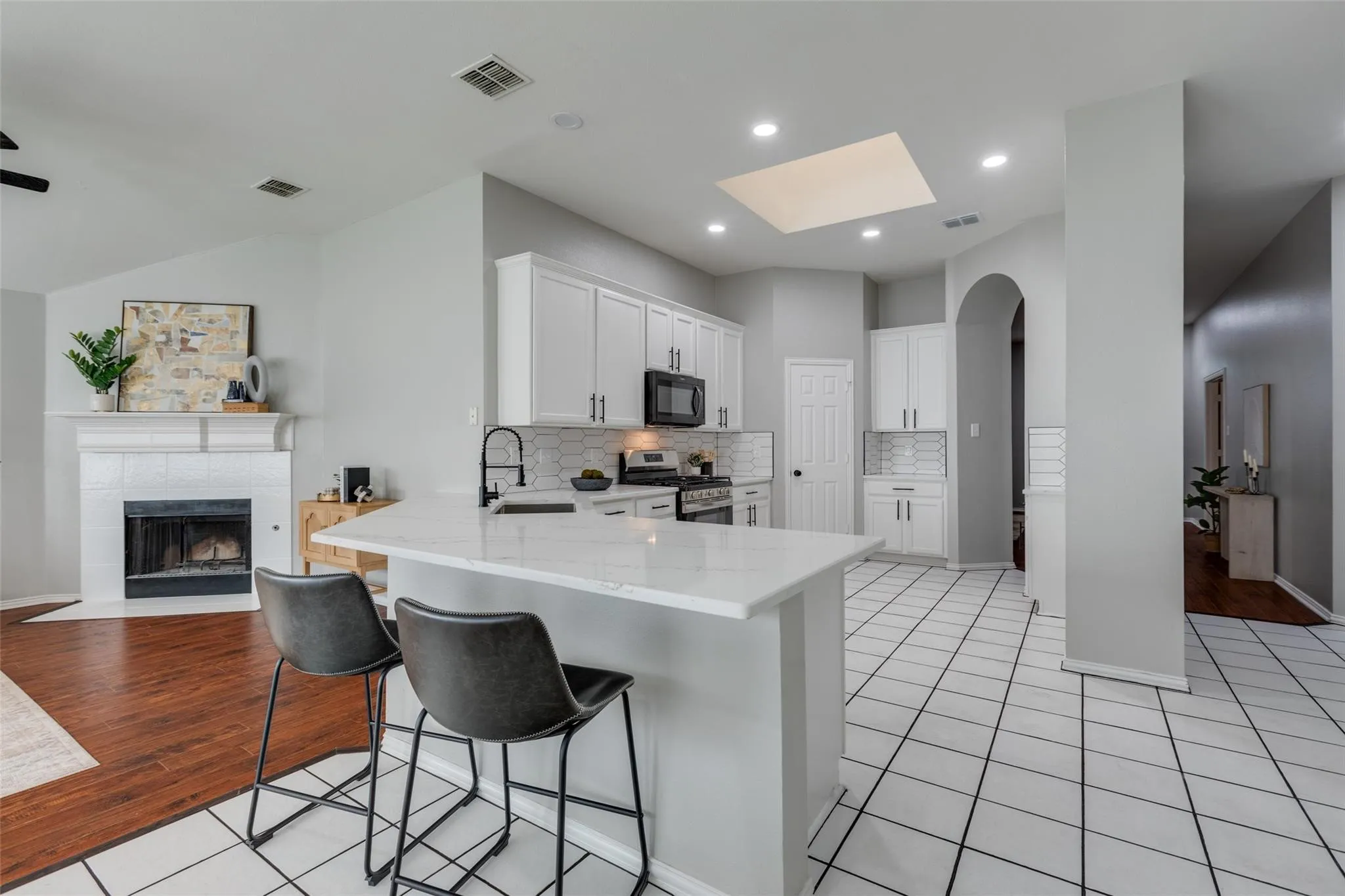 Open-concept kitchen featuring white cabinetry, quartz countertops, a kitchen island with bar seating, and a skylight