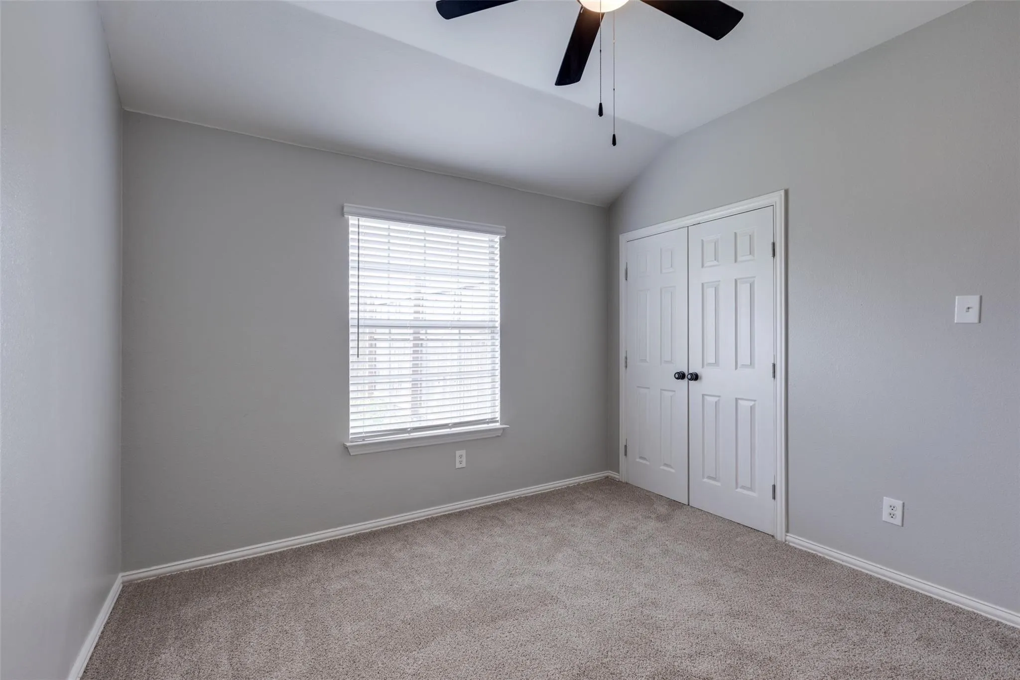 Carpeted room featuring a vaulted ceiling and a ceiling fan with light fixture