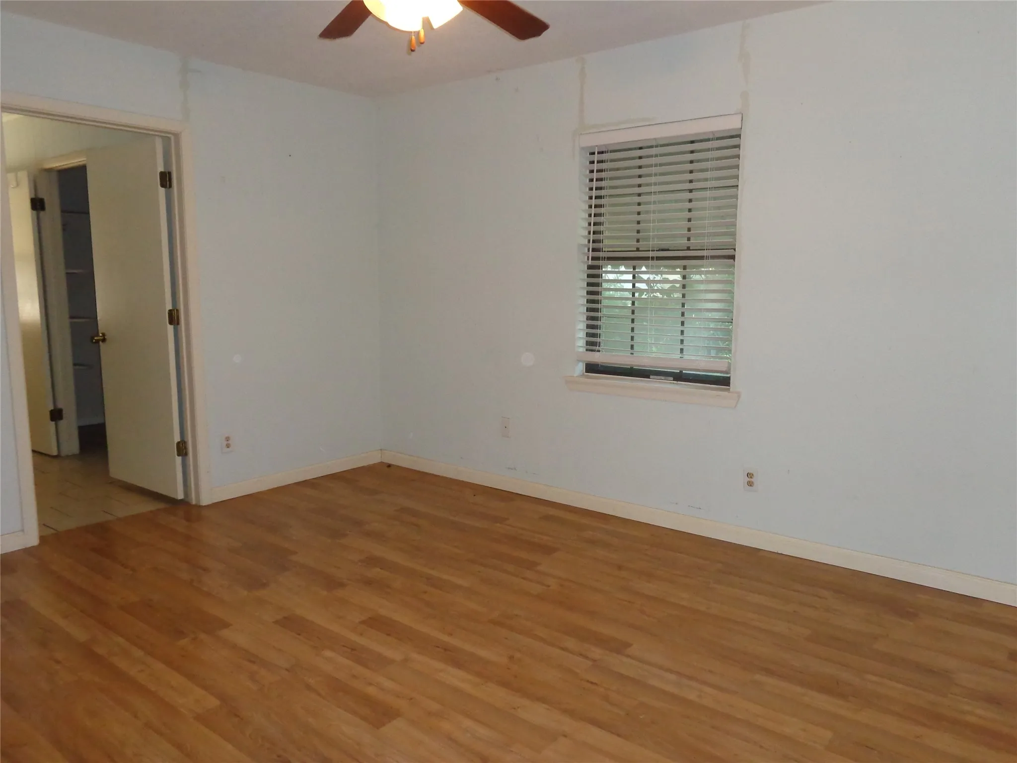 Wood-finish flooring throughout, ceiling fan with integrated lighting, and a single window with blinds