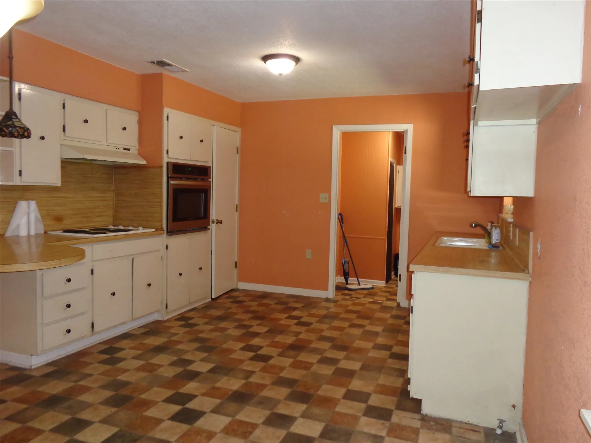 Kitchen with checkerboard flooring, built-in oven, white cabinetry, and a countertop range