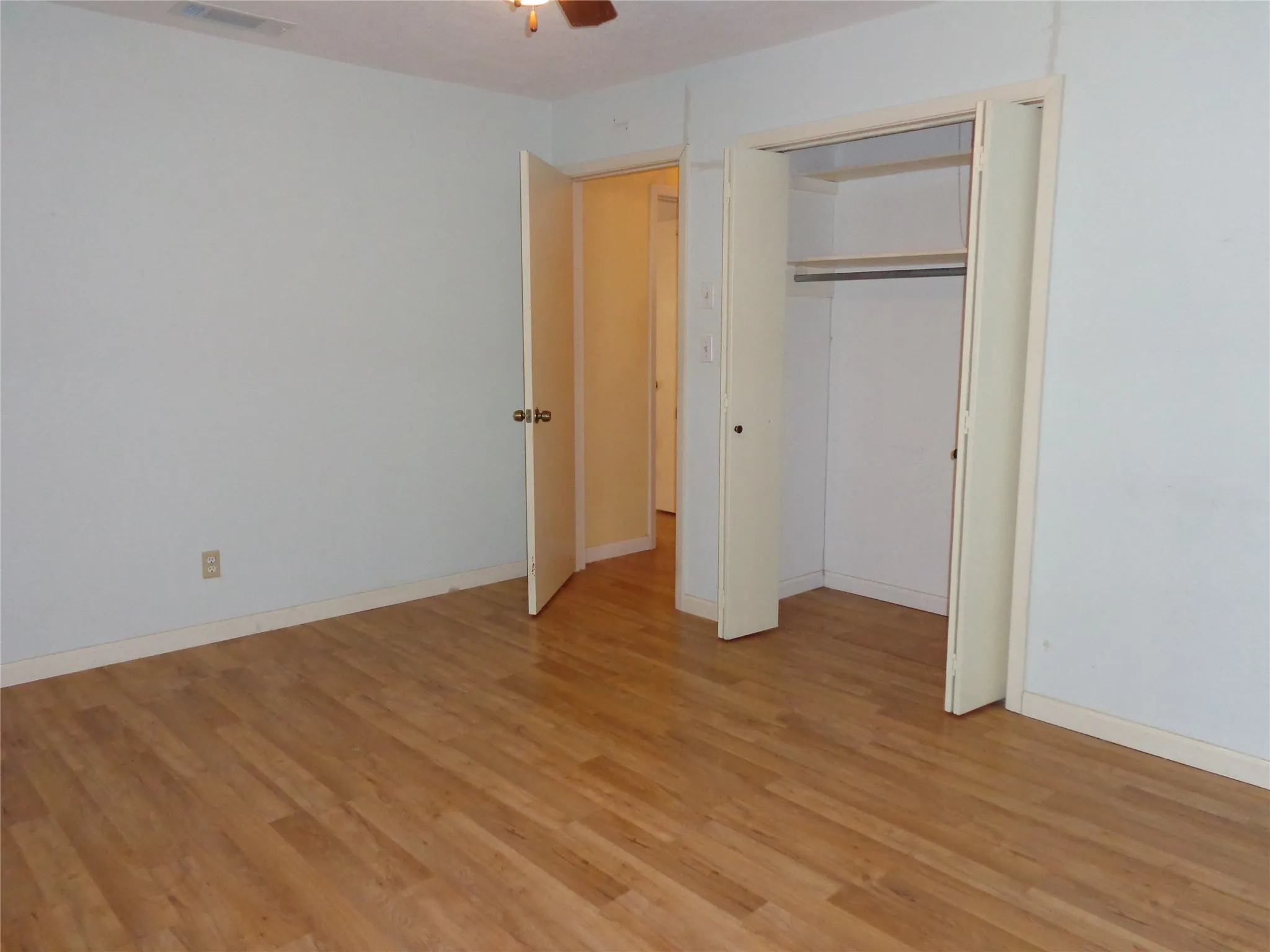 Wood-finish flooring, ceiling fan, and a built-in closet with shelving and hanging rod