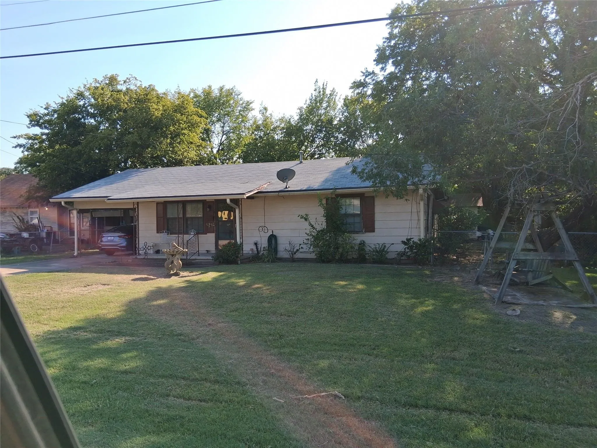 Single-story residence with a covered carport, pitched roof, and mature perimeter trees