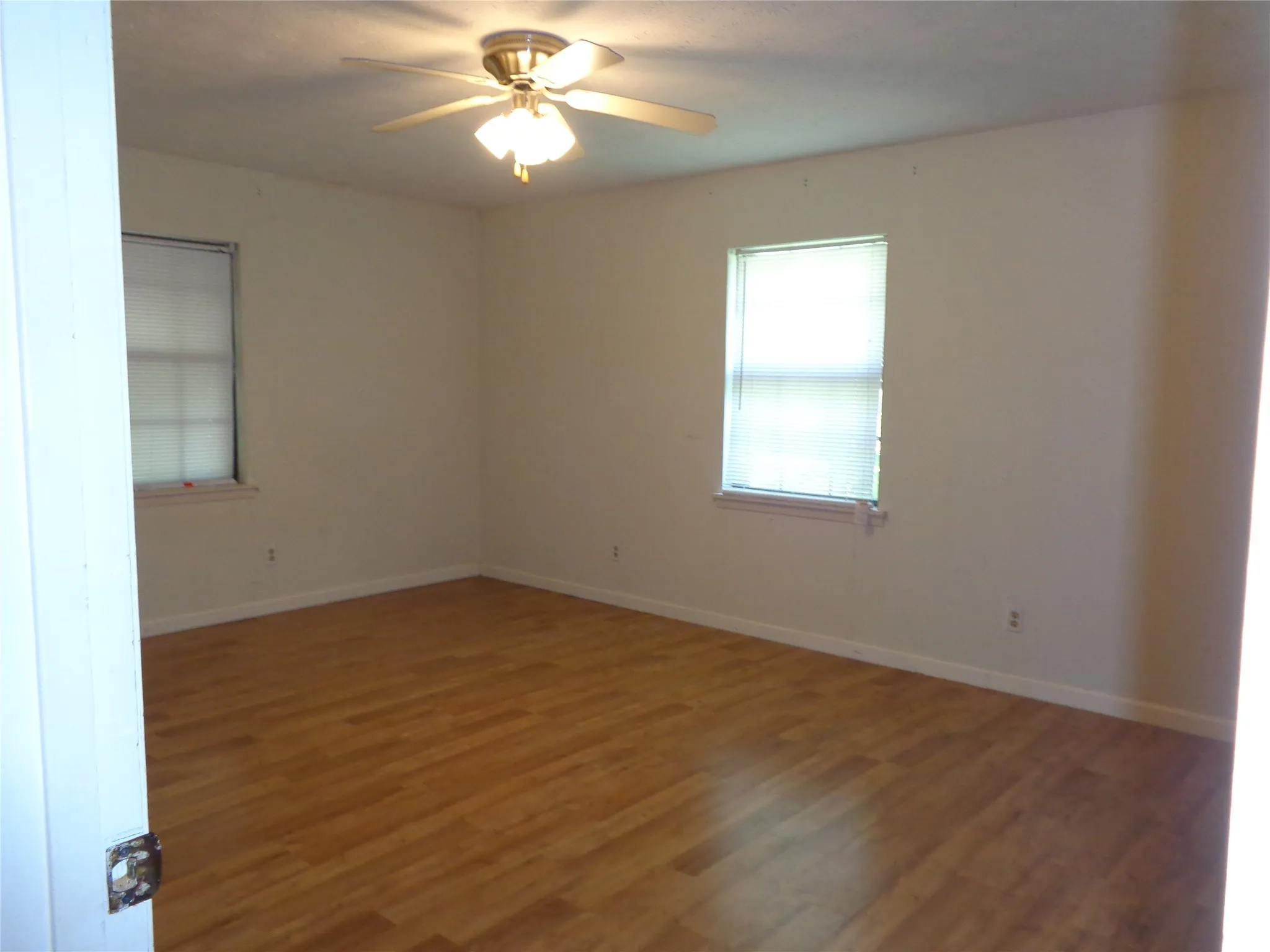 Wood-finish flooring and multiple windows with blinds, complemented by a ceiling fan light fixture