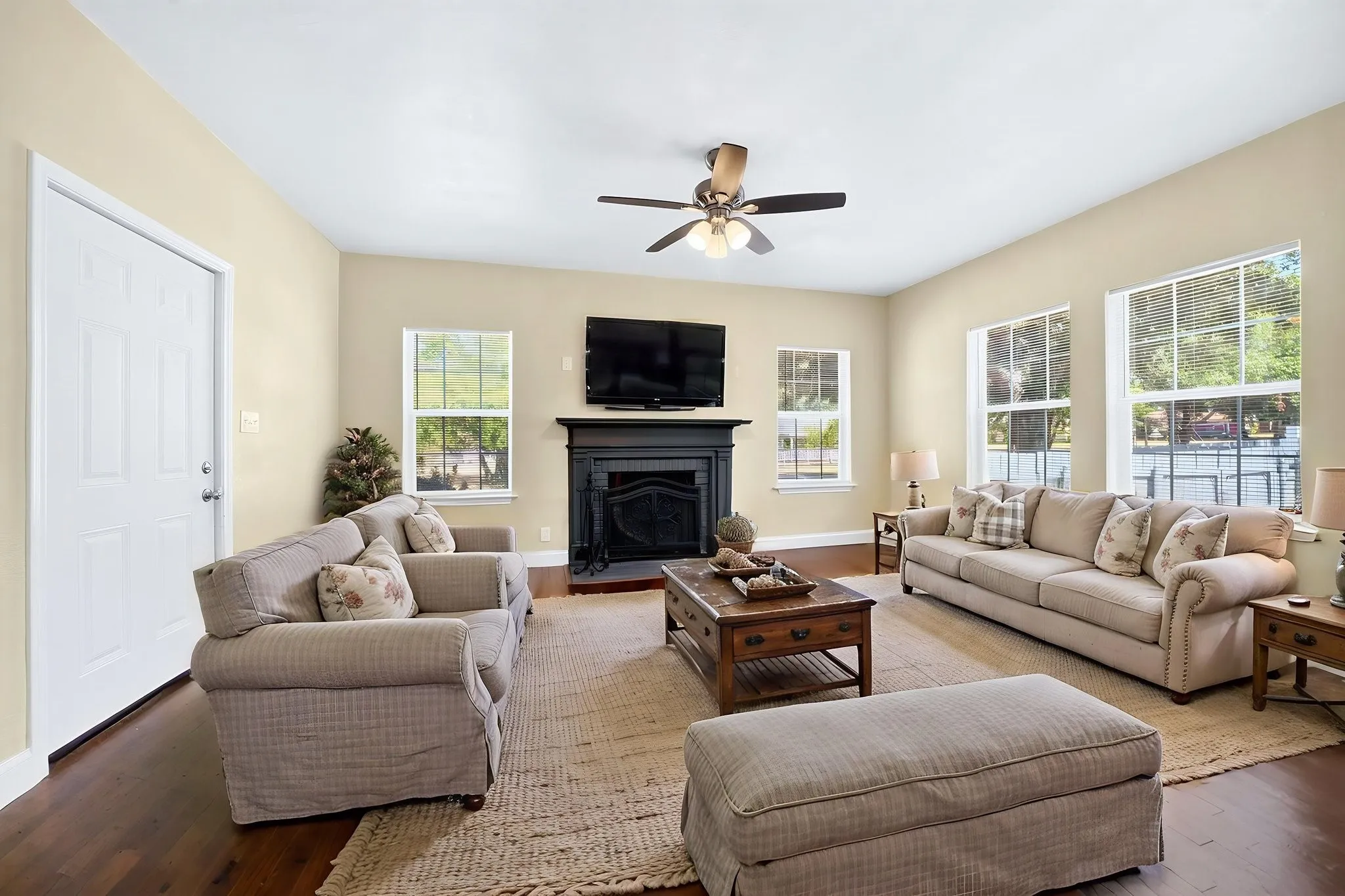 Hardwood flooring, painted walls, fireplace with mantel, ceiling fan, and multiple windows