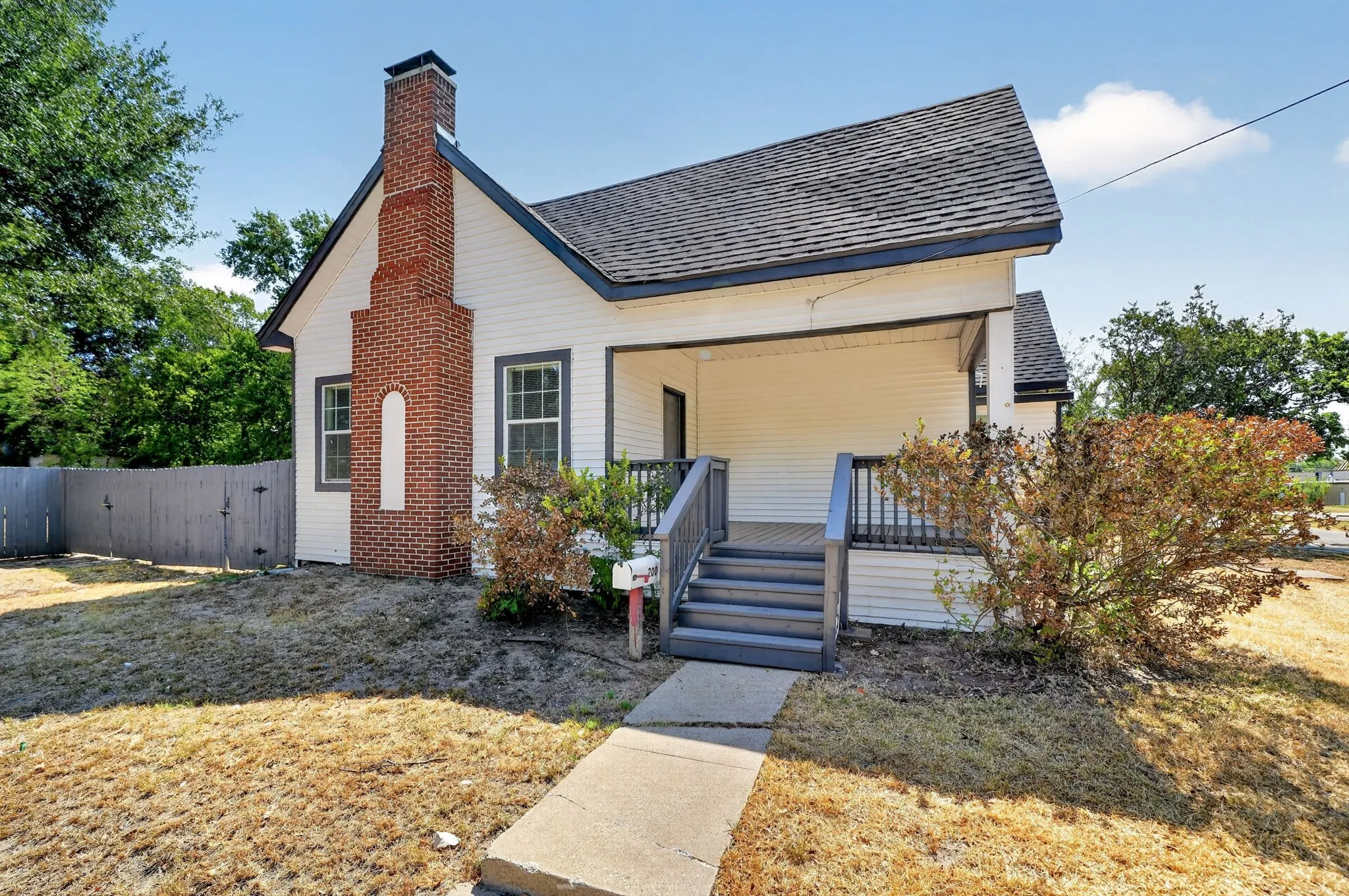 White siding exterior with a prominent brick chimney, covered front porch, and dark shingle roofing