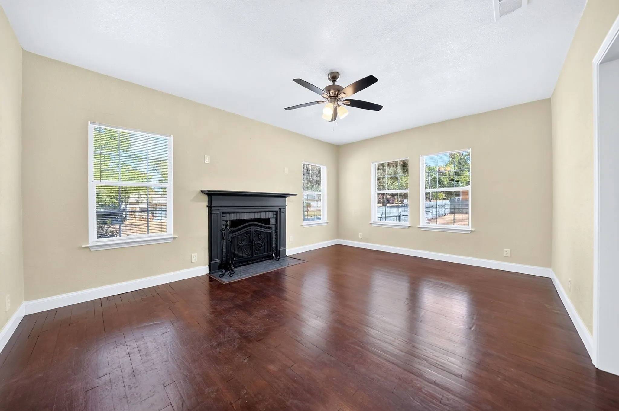 Spacious room featuring wood-finish flooring, a black mantle fireplace, multiple windows, and a ceiling fan with integrated lighting