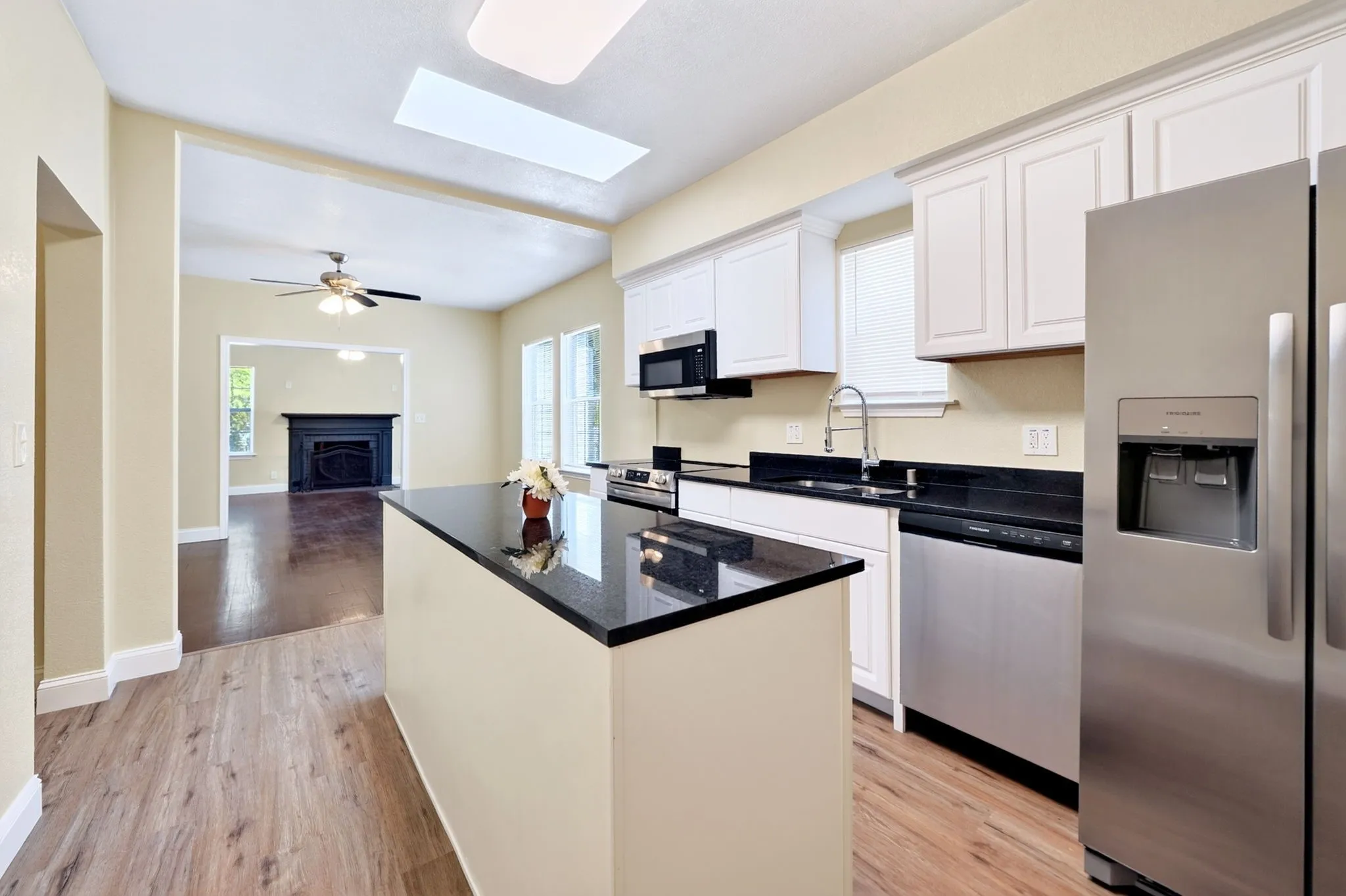 Kitchen featuring a central island with a dark countertop, white cabinetry, stainless steel appliances, and wood-finish flooring