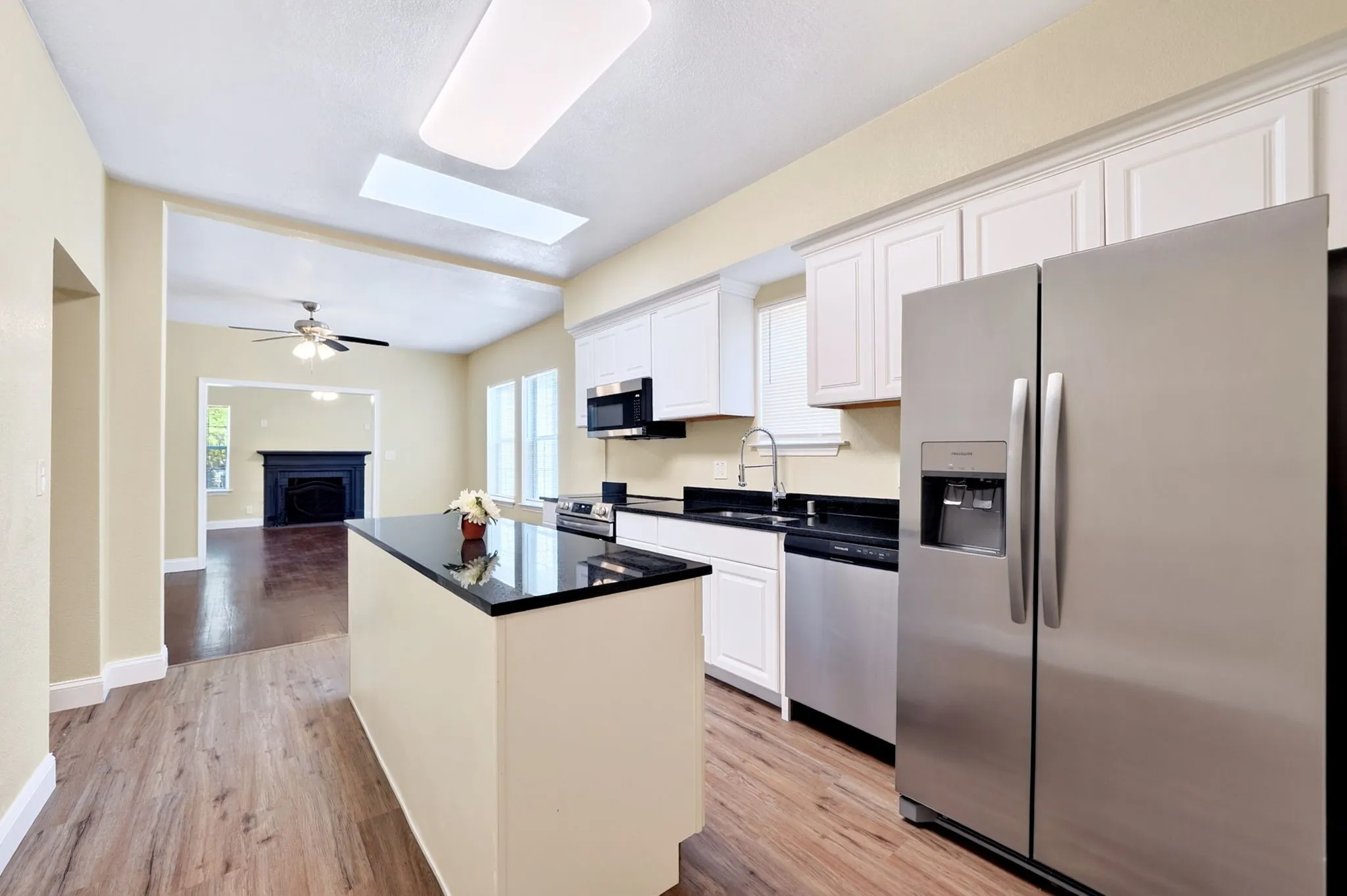 Kitchen featuring wood-finish flooring, white cabinetry, a central island with a dark countertop, and stainless steel appliances