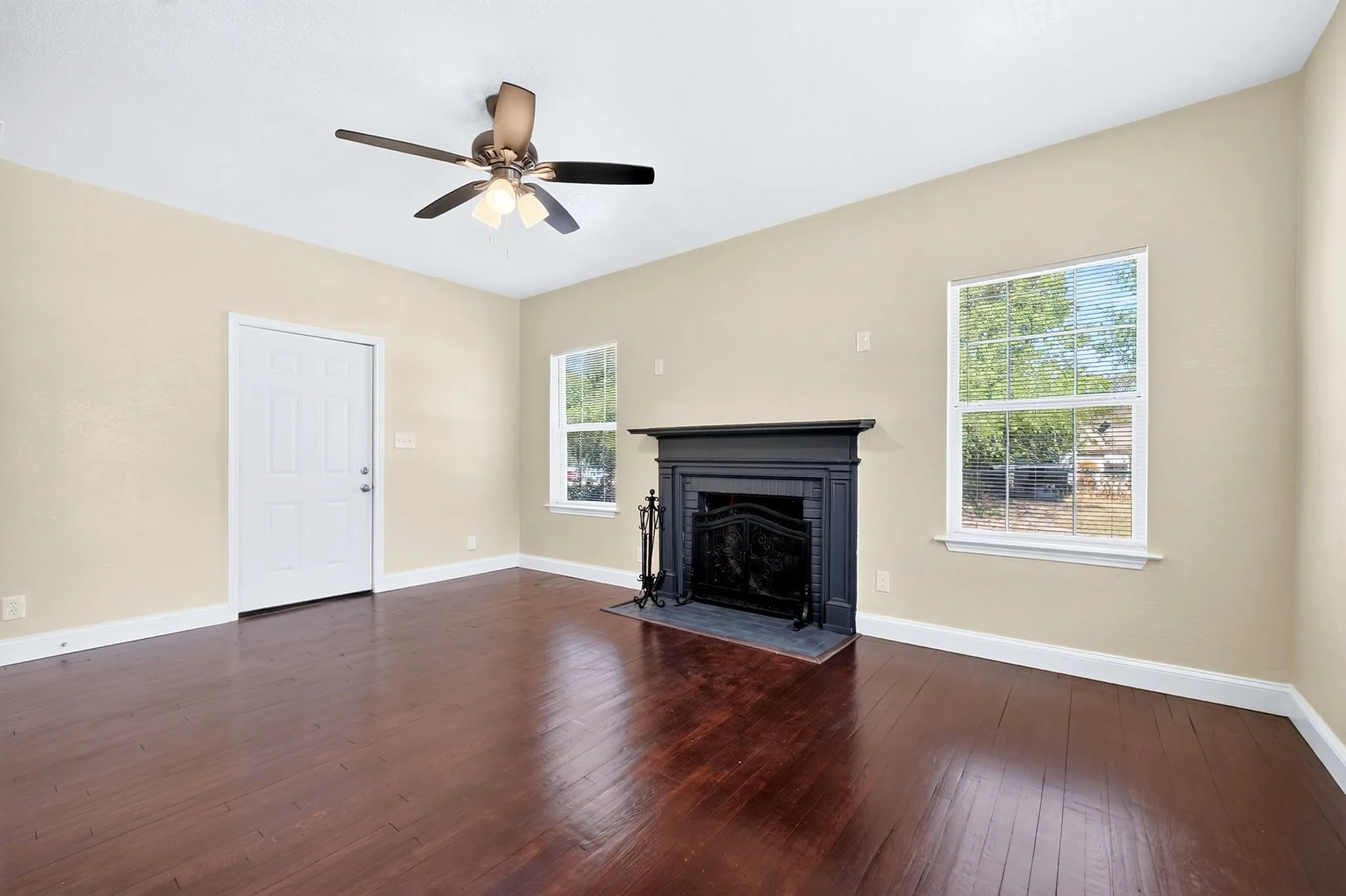 Spacious room featuring wood-finish flooring, a ceiling fan with integrated lighting, a decorative black fireplace, and two windows