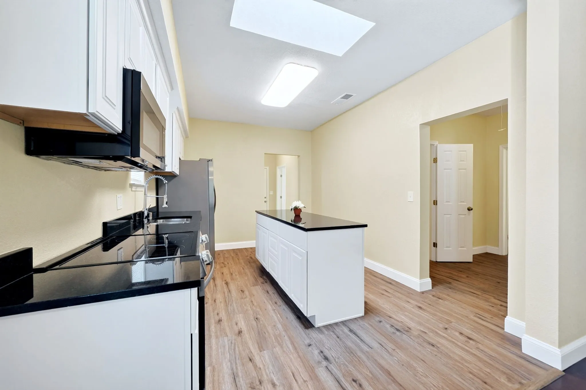 Kitchen featuring a central island, black countertops, wood-finish flooring, white cabinetry, and a skylight