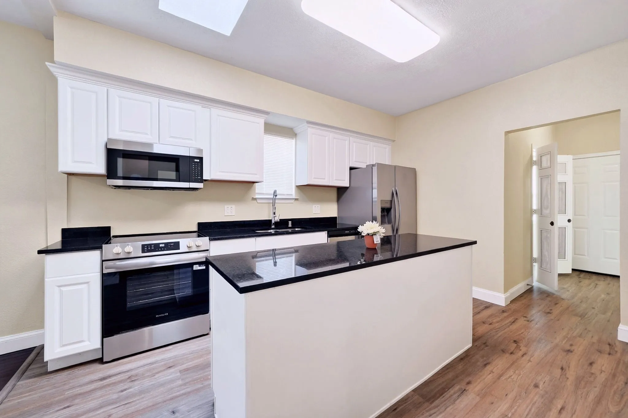 White cabinetry with black countertops, stainless steel appliances, and wood-finish flooring