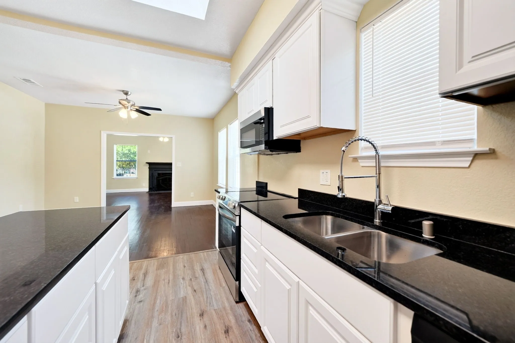 Kitchen featuring white cabinetry, dark stone countertops, a stainless steel double basin sink, and wood-finish flooring