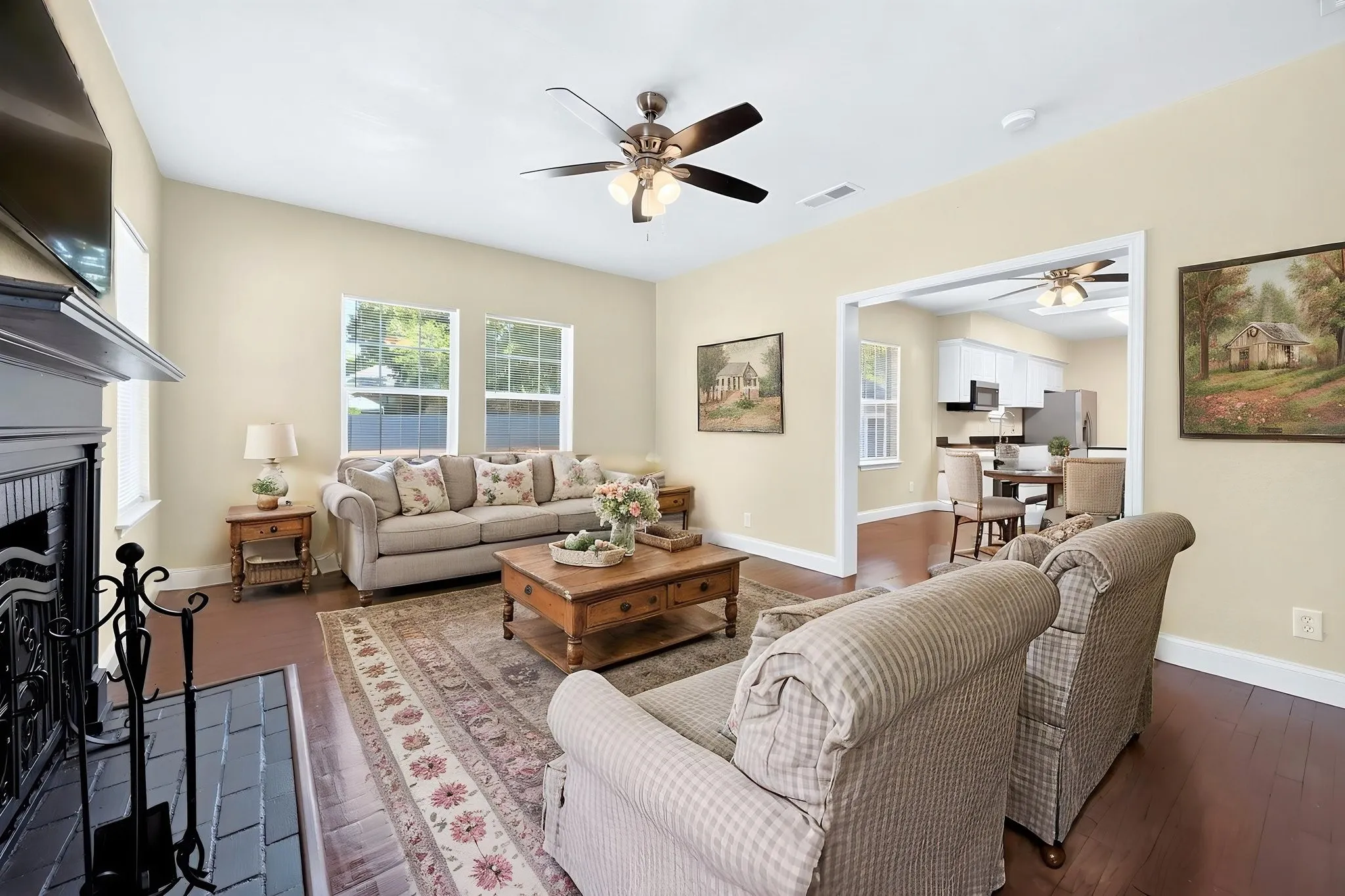Living area featuring a vaulted ceiling with a ceiling fan, dark wood-finish flooring, and a fireplace with a dark mantel
