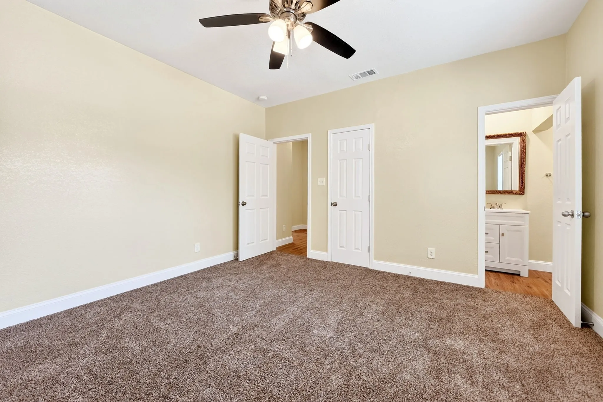 Carpeted room with a ceiling fan, white paneled doors, and direct access to an adjacent bathroom with a vanity and mirror