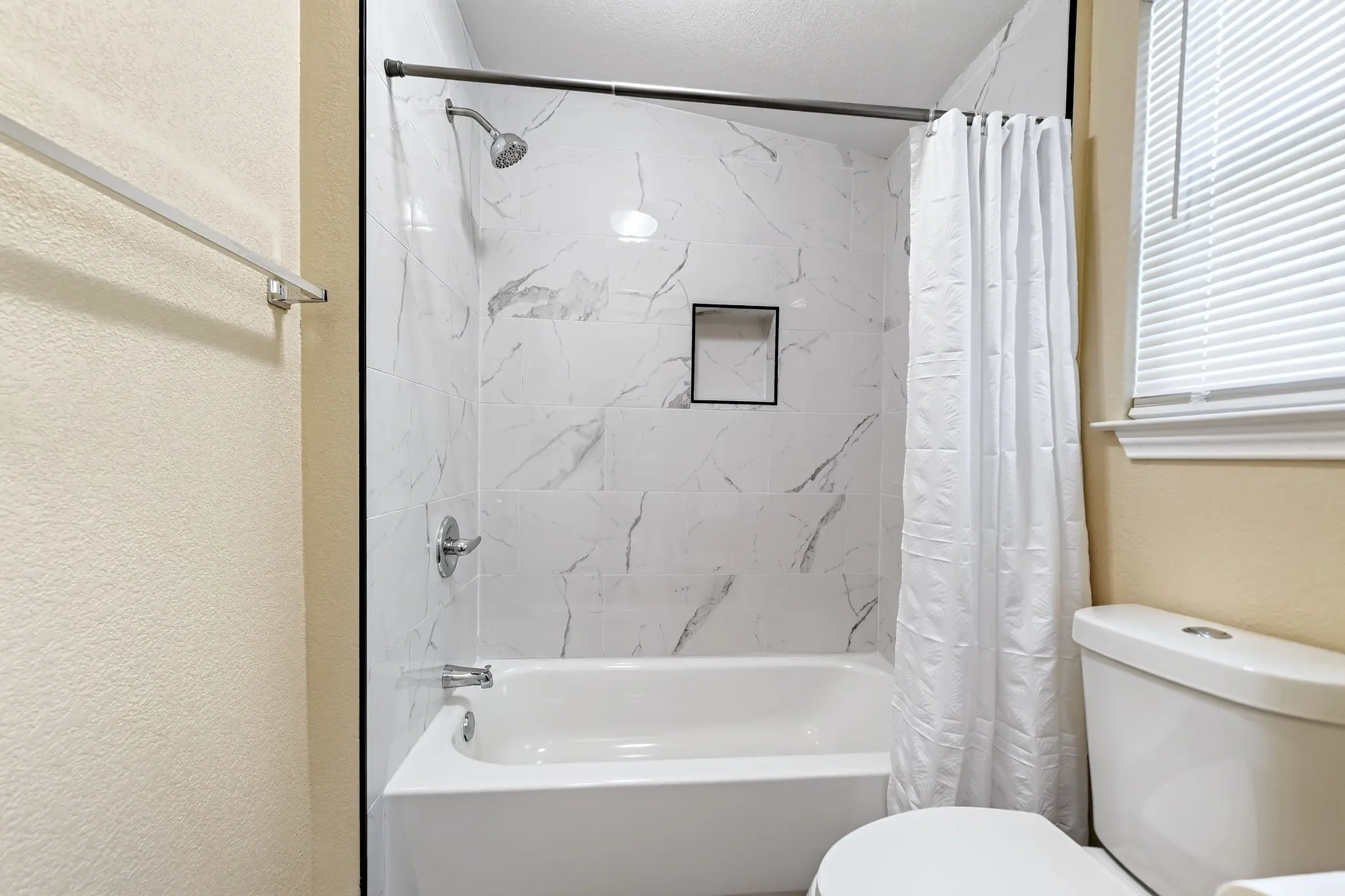 Bathtub with subway tile surround, built-in shower niche, and chrome fixtures