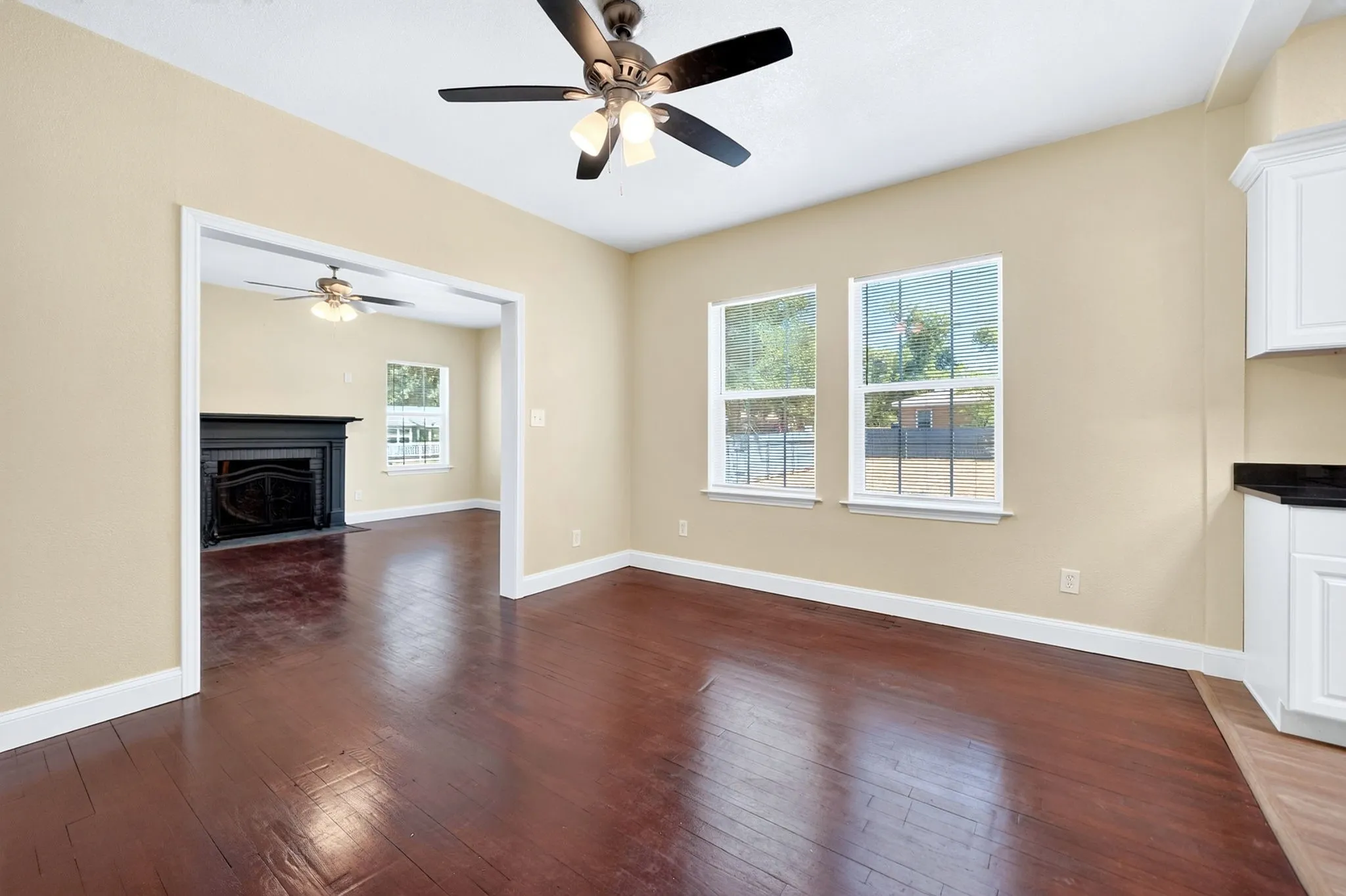 Hardwood flooring, ceiling fan, white cabinetry, dark countertop, and multiple windows