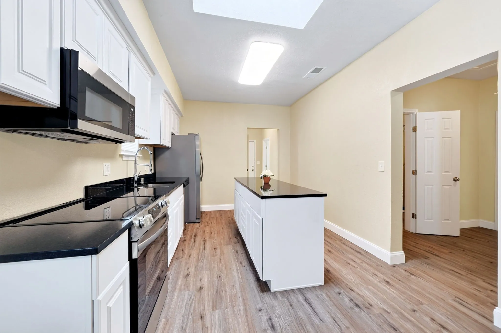 Kitchen featuring white cabinetry, black countertops, stainless steel appliances, a central island, and wood-finish flooring