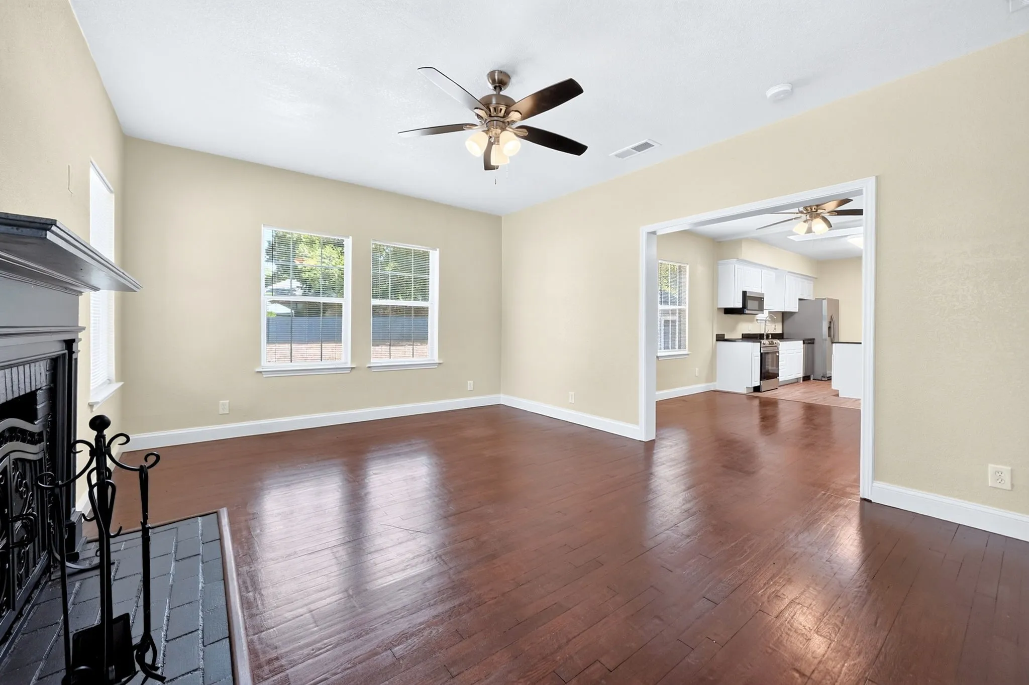 Spacious living area featuring dark wood-finish flooring, a decorative fireplace with a mantel, and an exposed beam ceiling
