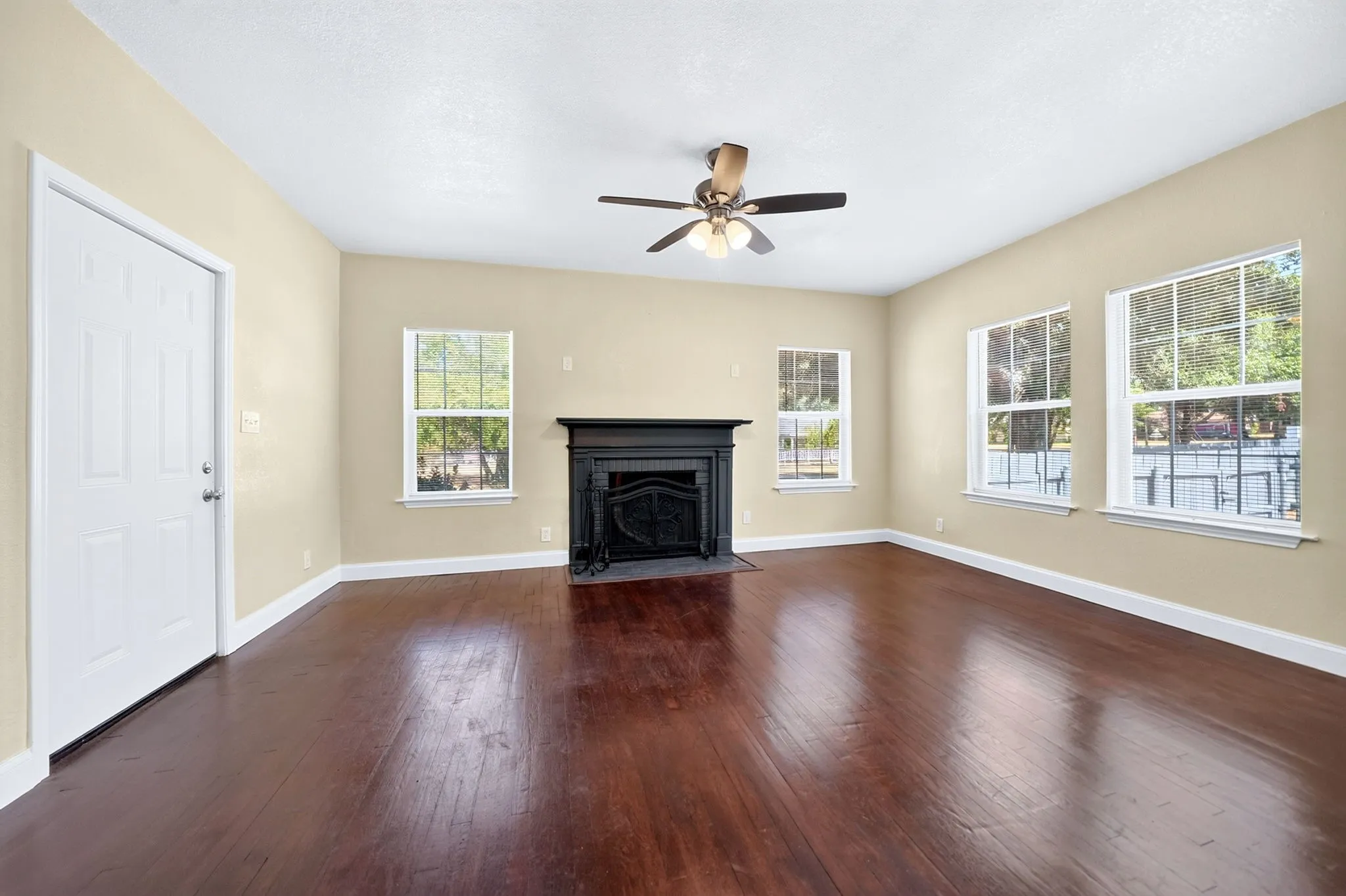Wood-finish flooring, a ceiling fan with integrated lighting, multiple windows, a black fireplace, and a white paneled door