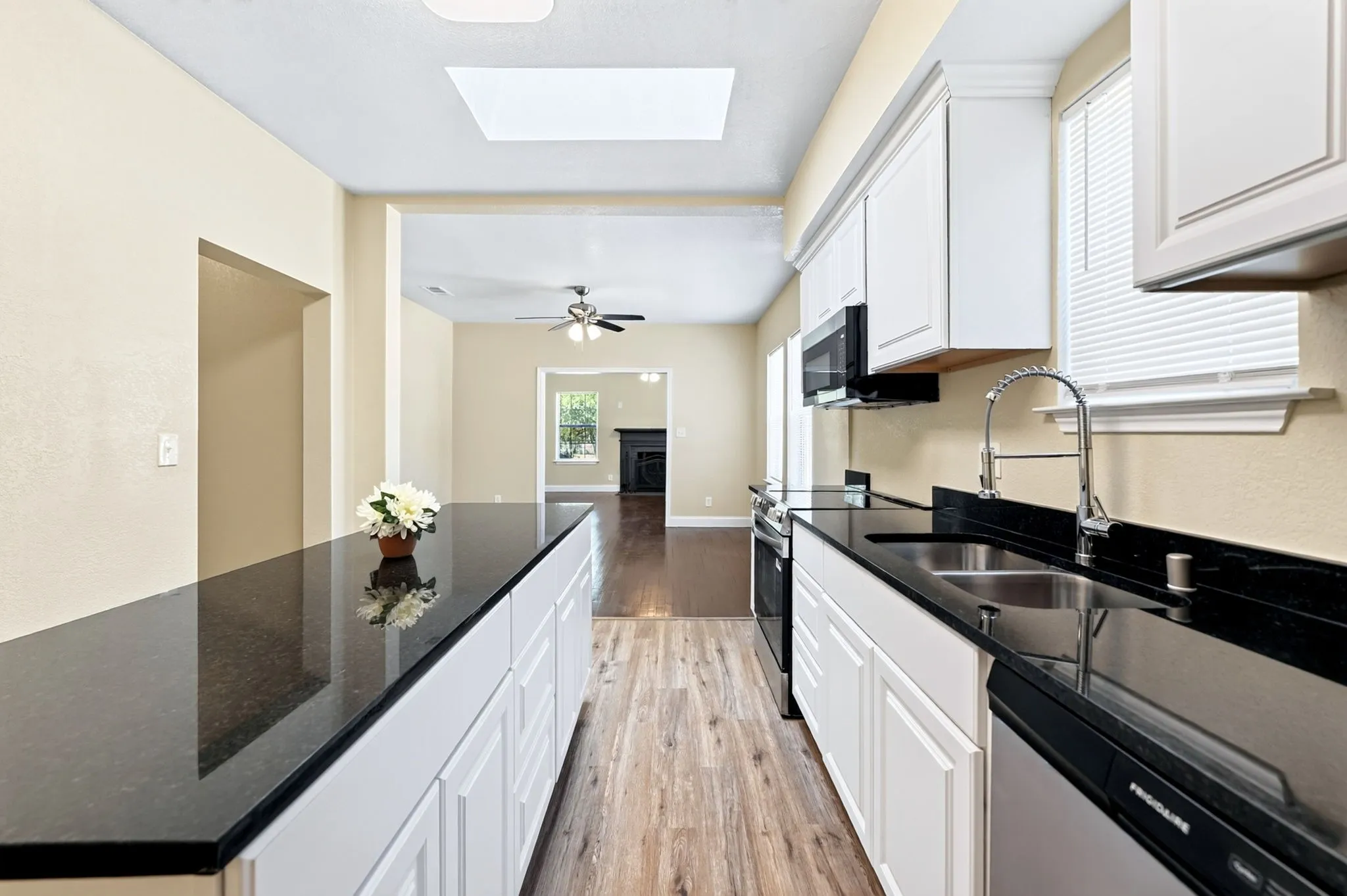 Kitchen featuring white cabinetry, black countertops, stainless steel appliances, and wood-finish flooring