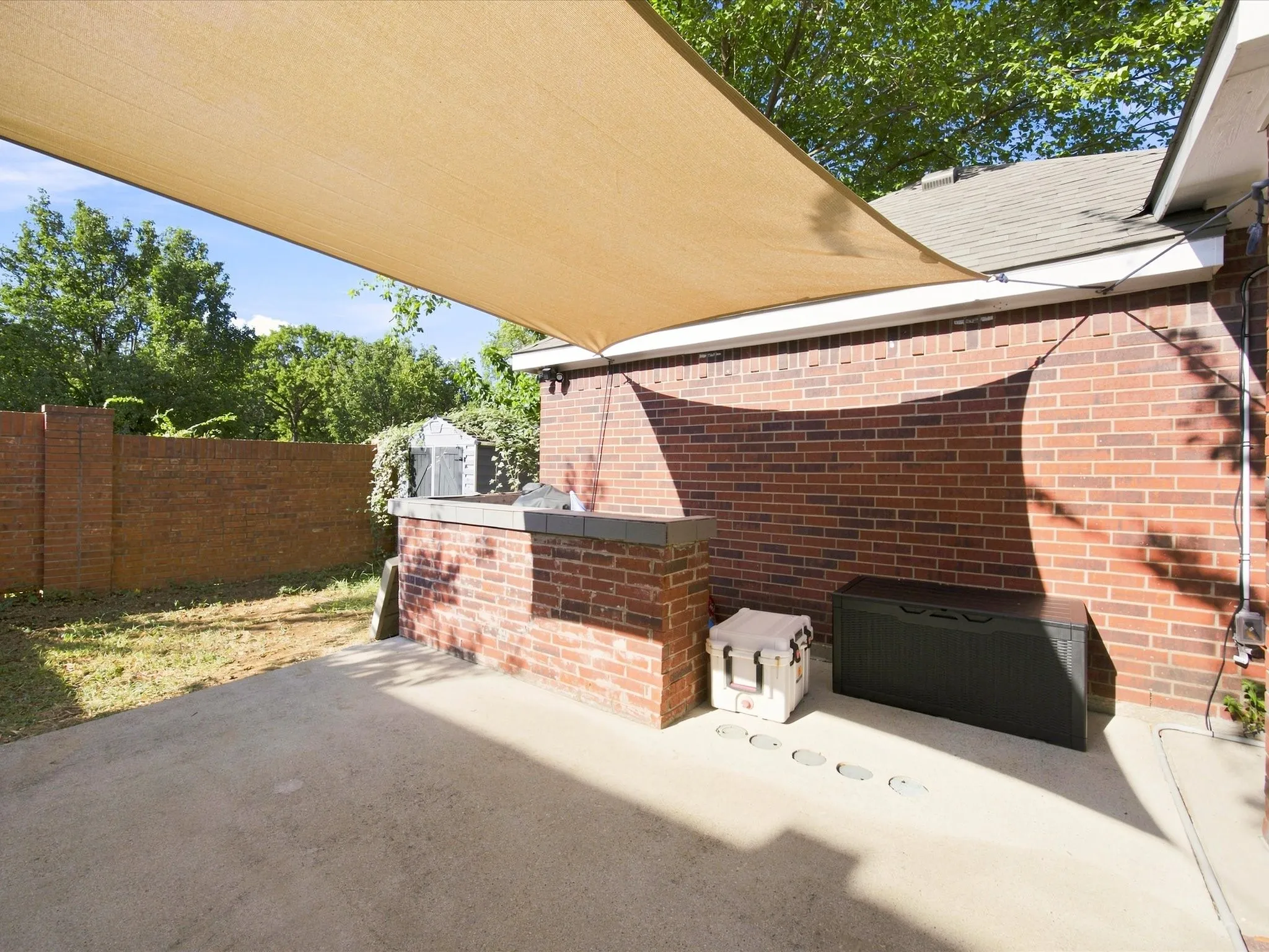 Concrete patio with an overhead shade sail, brick exterior wall, and a built-in brick and concrete bar
